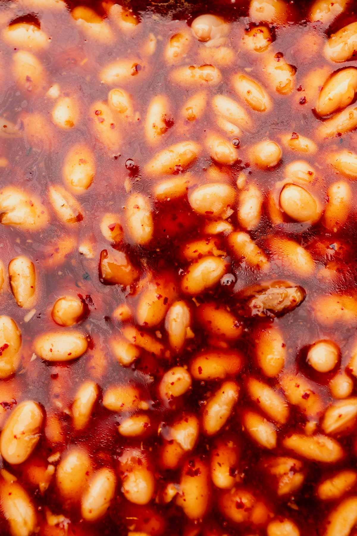 Close-up of a textured surface featuring white beans in a thick, reddish Korean BBQ sauce.