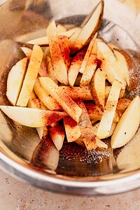 Potato wedges in a metal bowl topped with paprika, salt, and pepper—these oven baked french fries are ready to be mixed or cooked to crispy perfection.