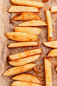 Potato wedges coated in seasoning are arranged on a sheet of parchment paper, ready for baking into crispy oven baked french fries.