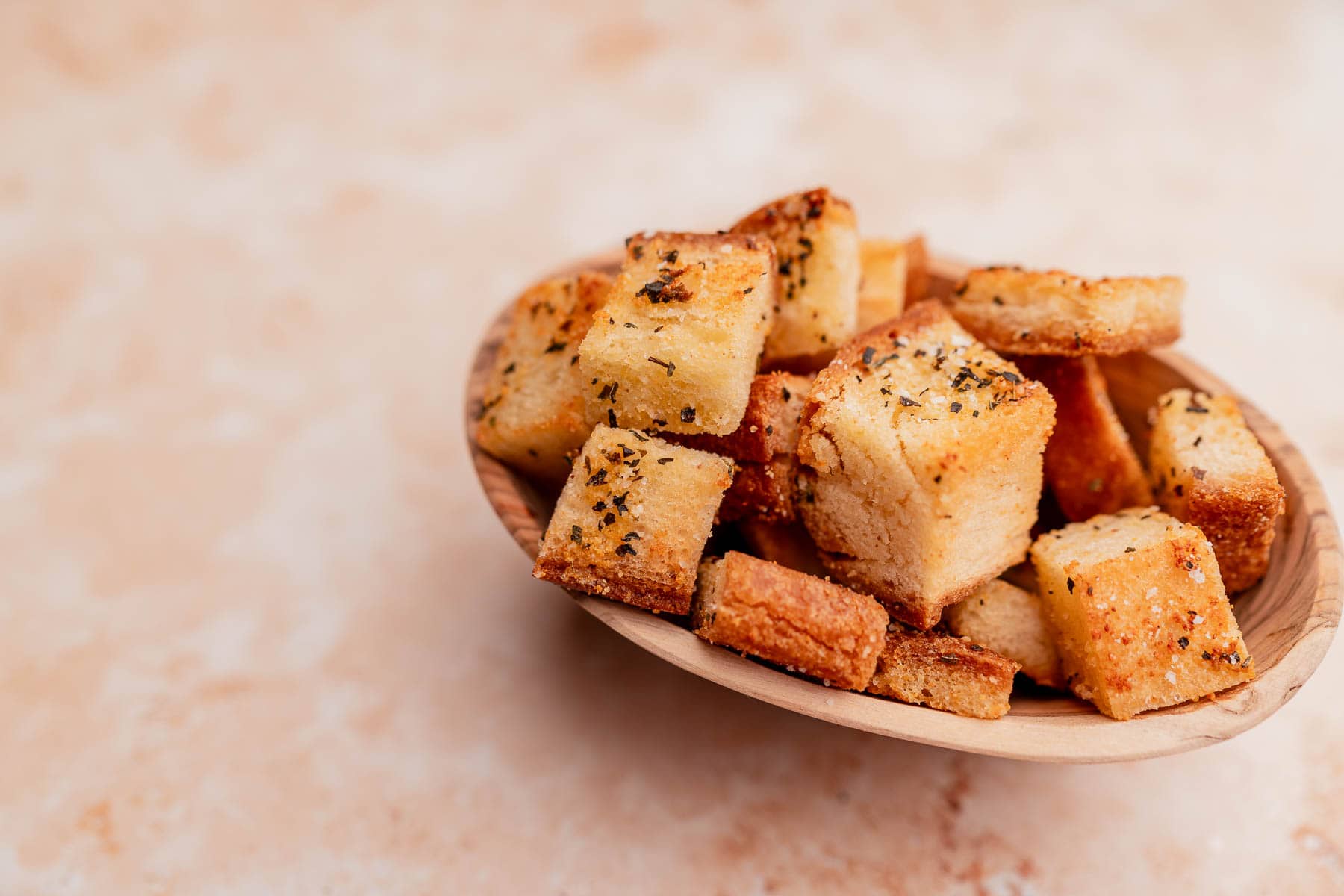 A bowl filled with golden-brown, seasoned gluten-free croutons is shown against a neutral background.