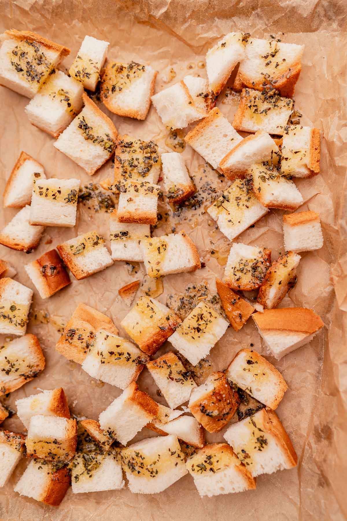 Small, evenly cut gluten free croutons seasoned with herbs, spread on a parchment-lined baking sheet.