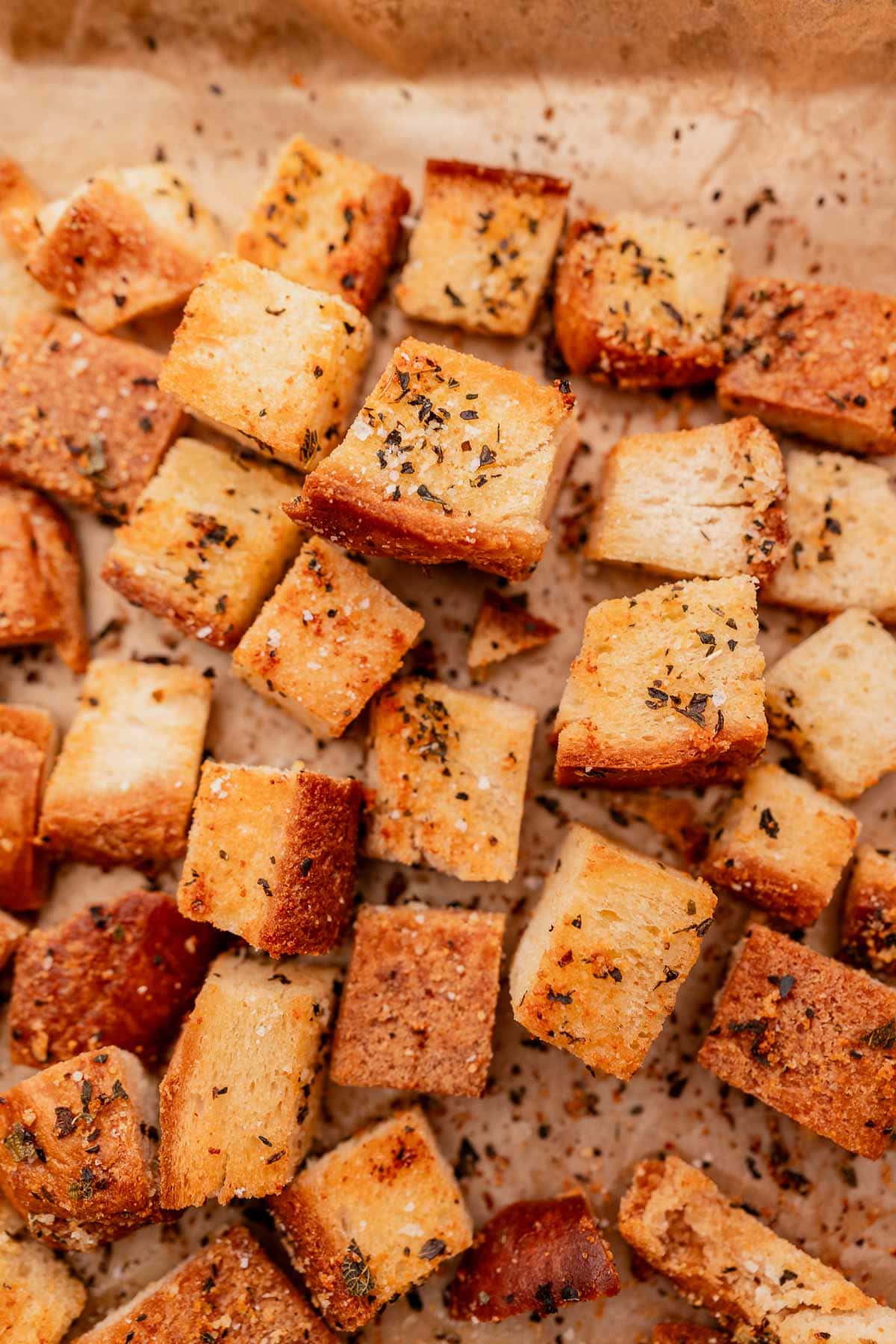 A close-up photo of gluten free croutons on a baking sheet, showing the texture and seasoning on the small, toasted bread cubes.