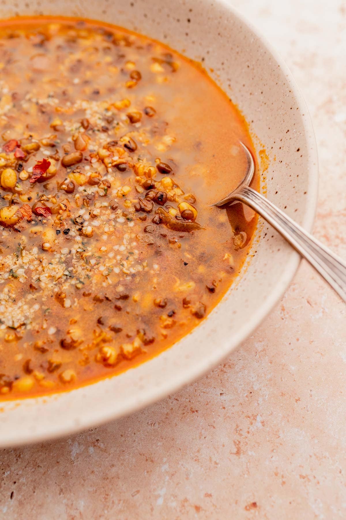 A close shot of a silver spoon scooping mung bean soup out of a large tan bowl.