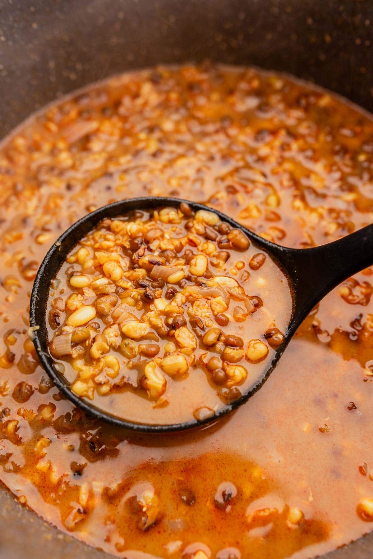 A ladle scoops freshly cooked mung bean soup from a large pot.