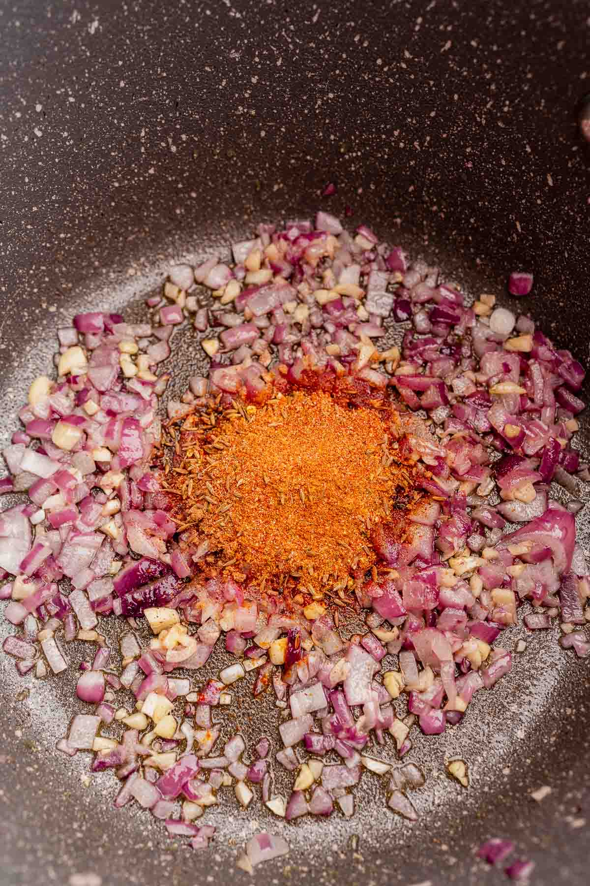 Sauteed onions and orange spices in a pot.