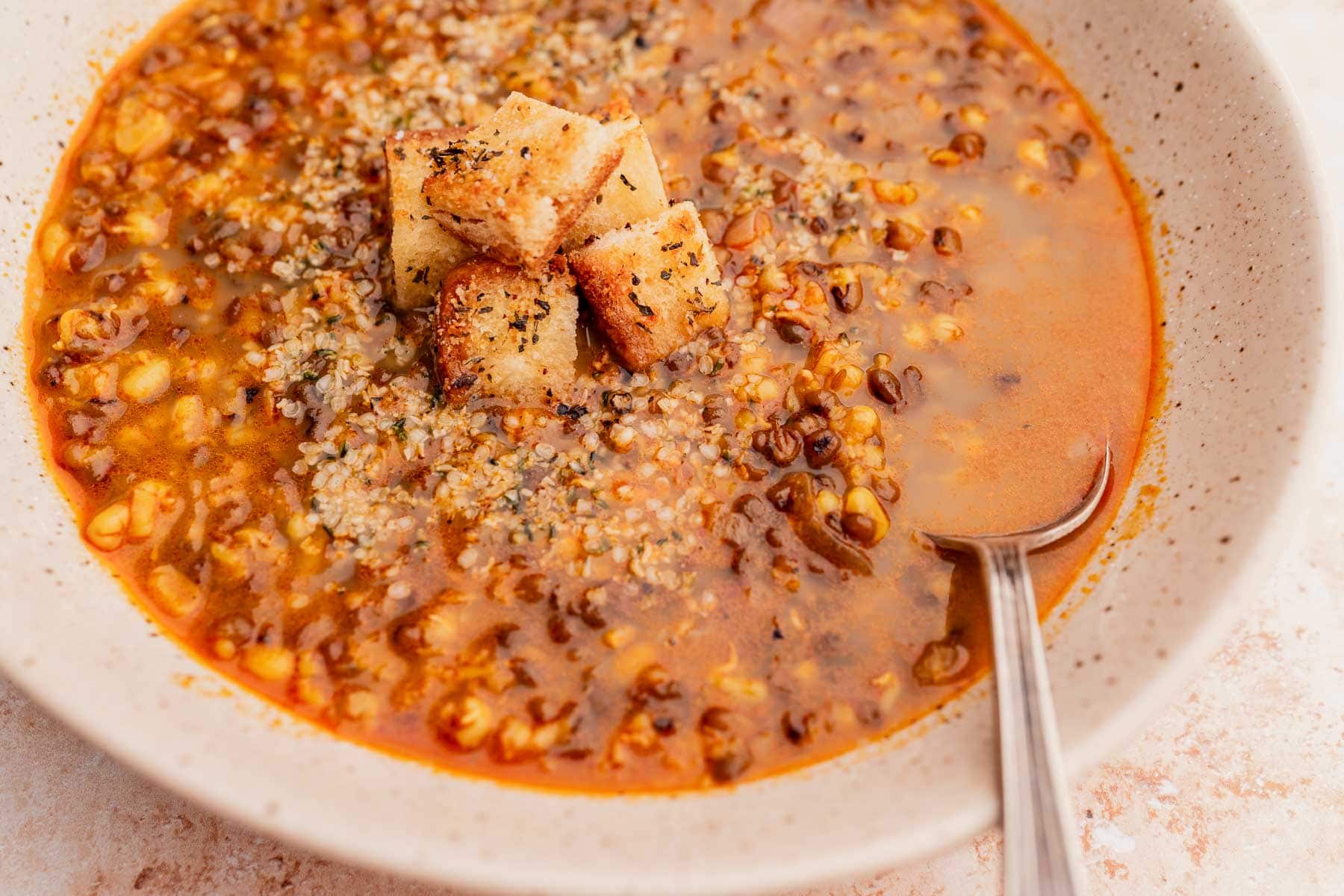 A big bowl of mung bean soup with a silver spoon and a croutons garnish.
