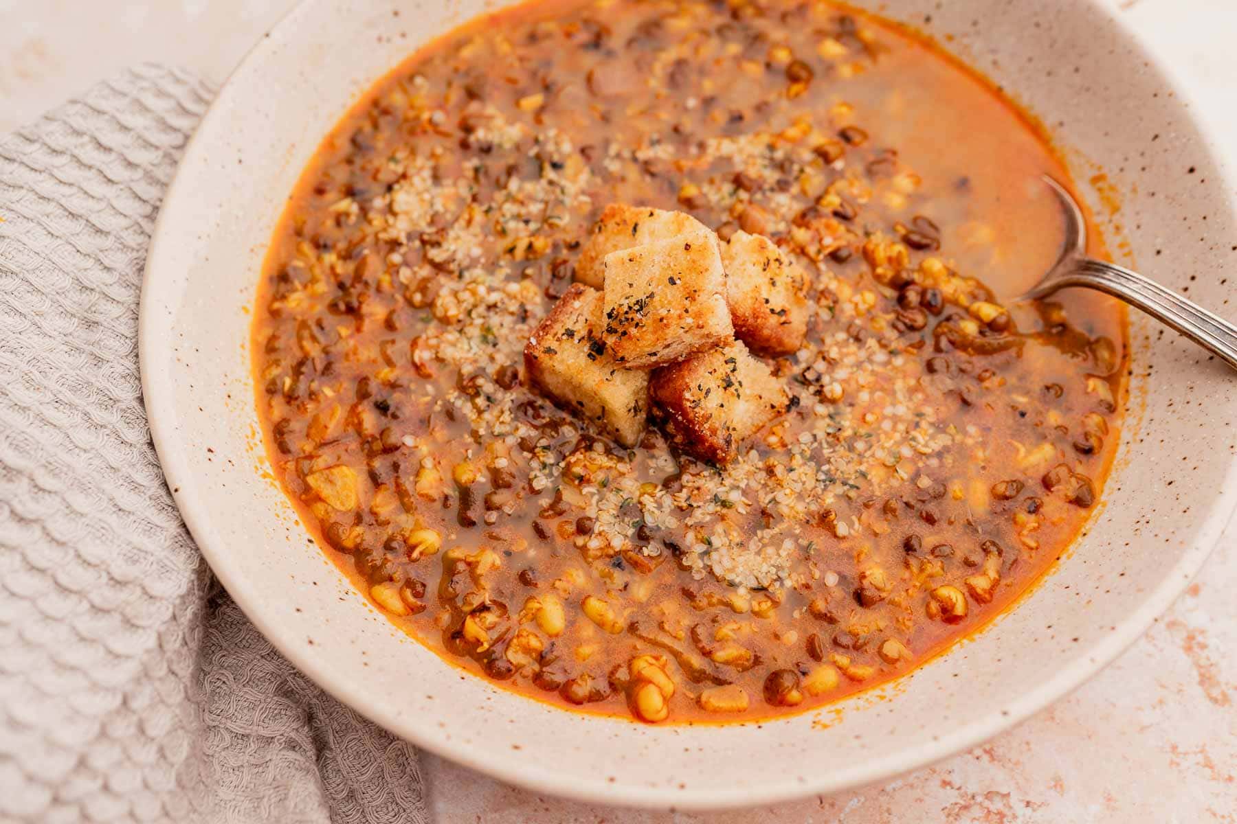 A small speckled ceramic bowl filled with mung bean soup garnished with croutons and seeds.