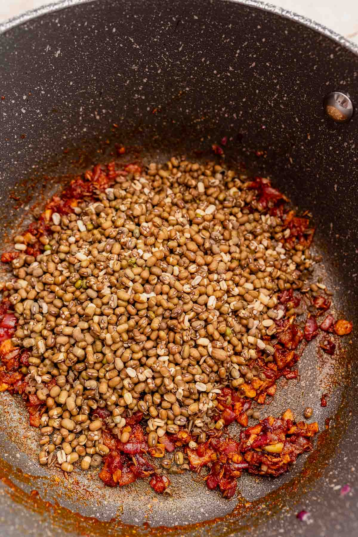 Sauteed onions and spices with uncooked sprouted mung beans in a pot.