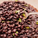 A spoon rests in a dish filled with cooked black beans garnished with bits of fresh cilantro.
