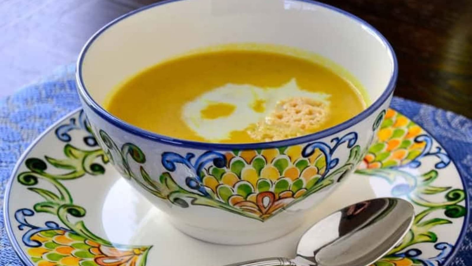 A bowl of butternut squash soup with a spoon on a colorful blue and white plate.