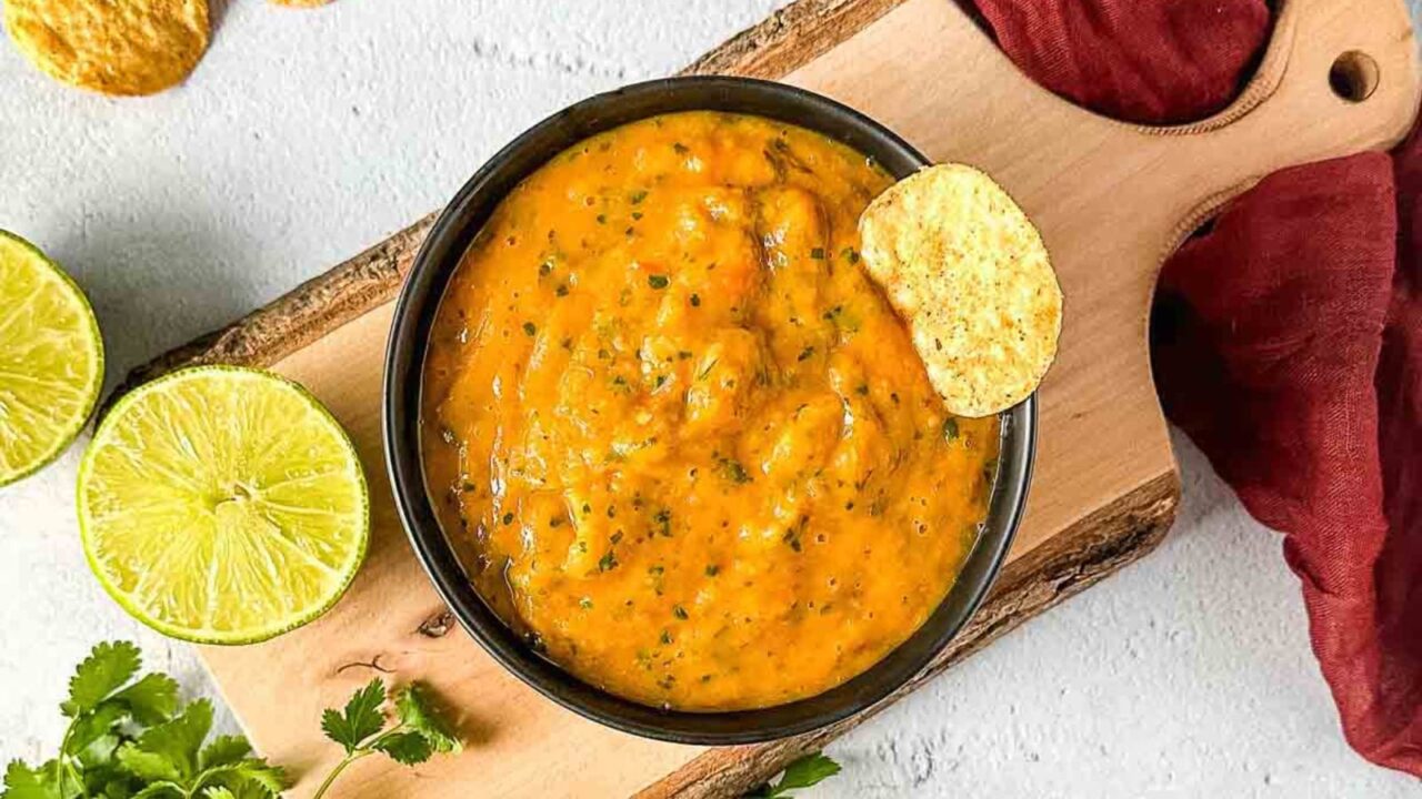 Roasted mango habanero salsa on a wooden cutting board surrounded by lime and cilantro.