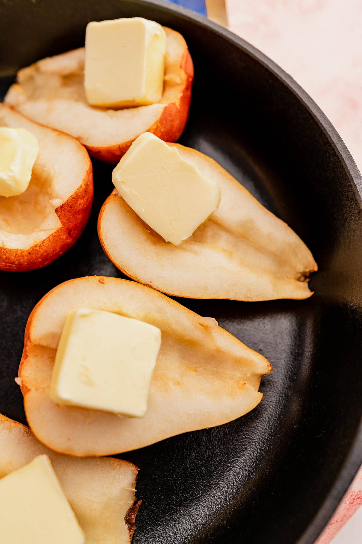 Halved pears in a black pan, each topped with a square of butter, are elevated to new heights when drizzled with chocolate balsamic glaze.