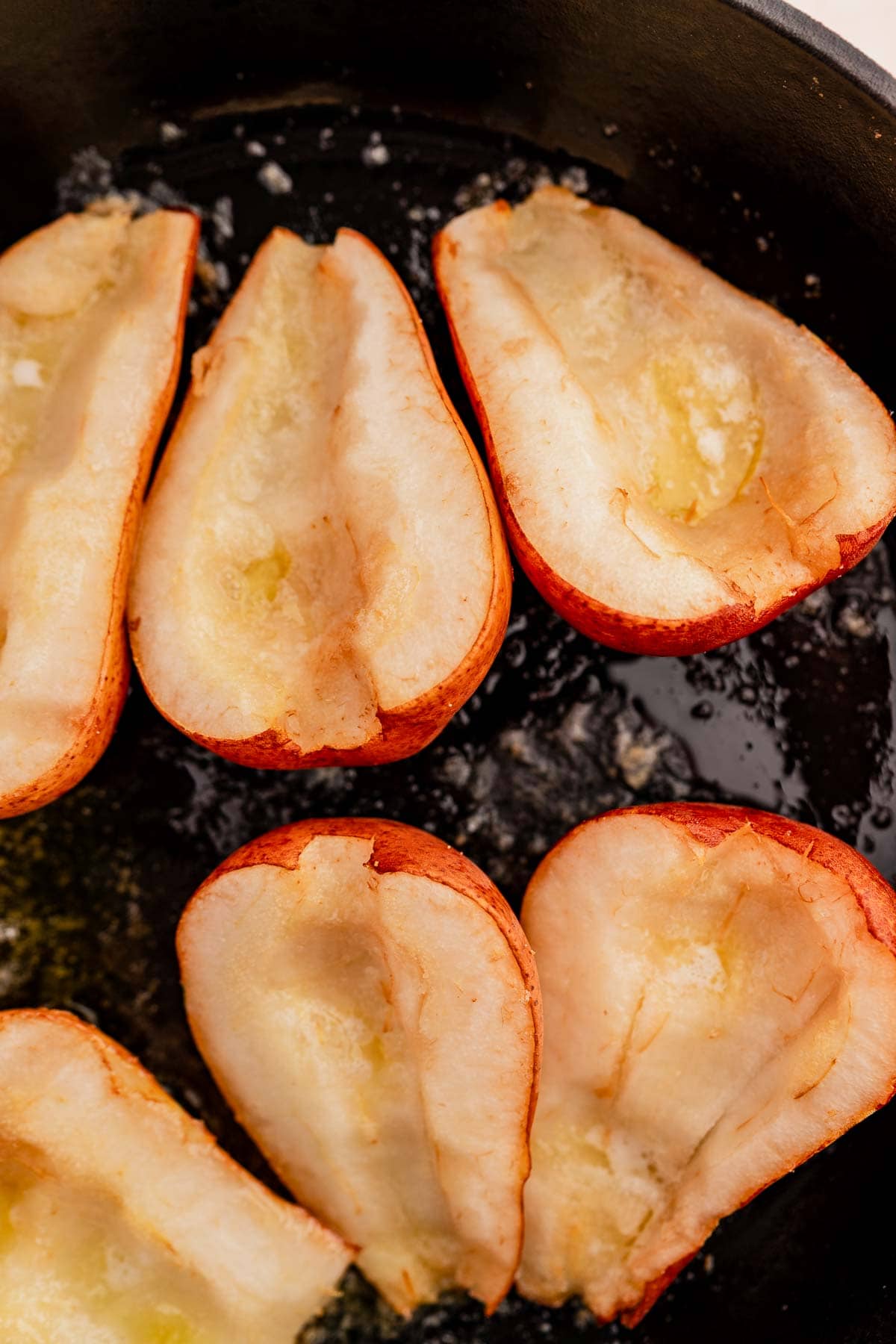 Halved pears with butter in a black skillet, ready to be transformed into chocolate balsamic glazed pears.