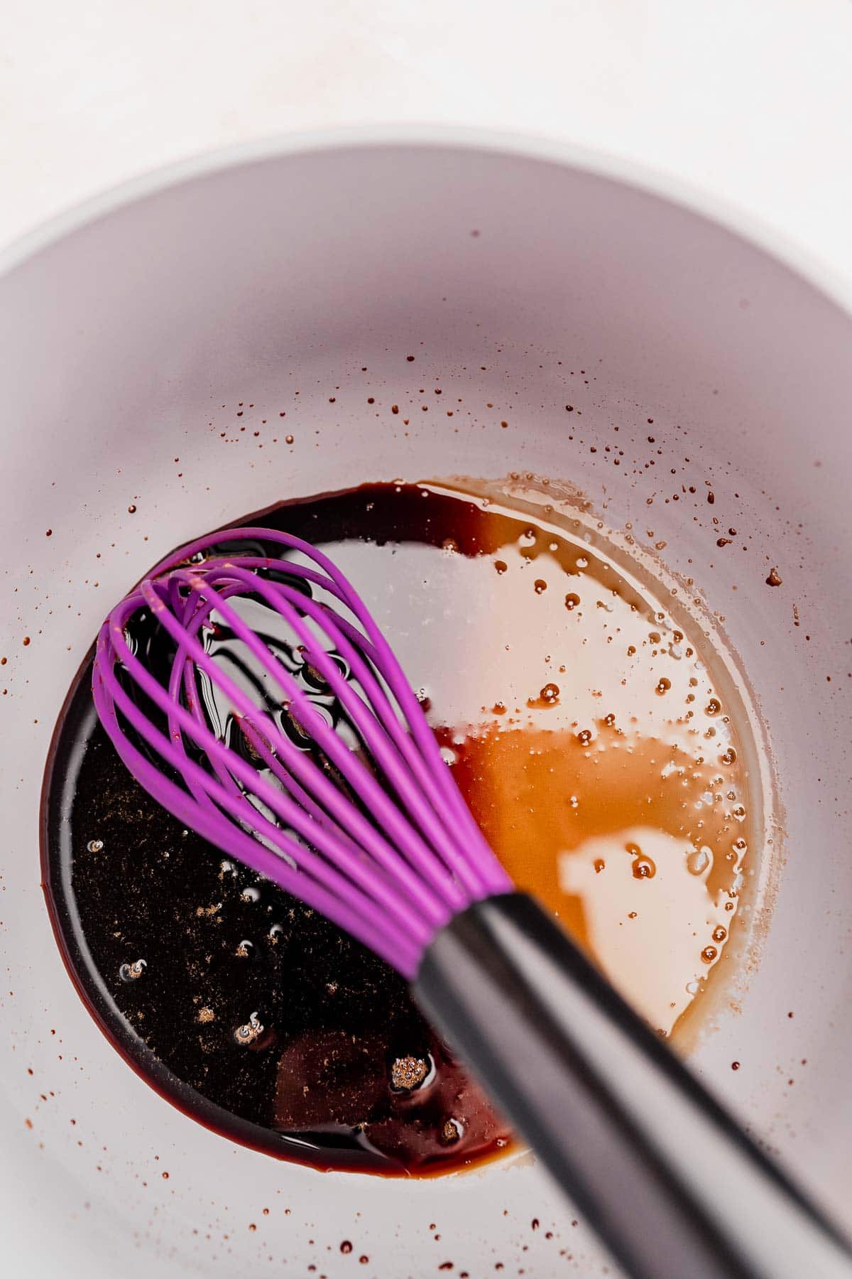 A purple whisk in a white bowl mixing dark chocolate ingredients for a rich balsamic glazed pears recipe.