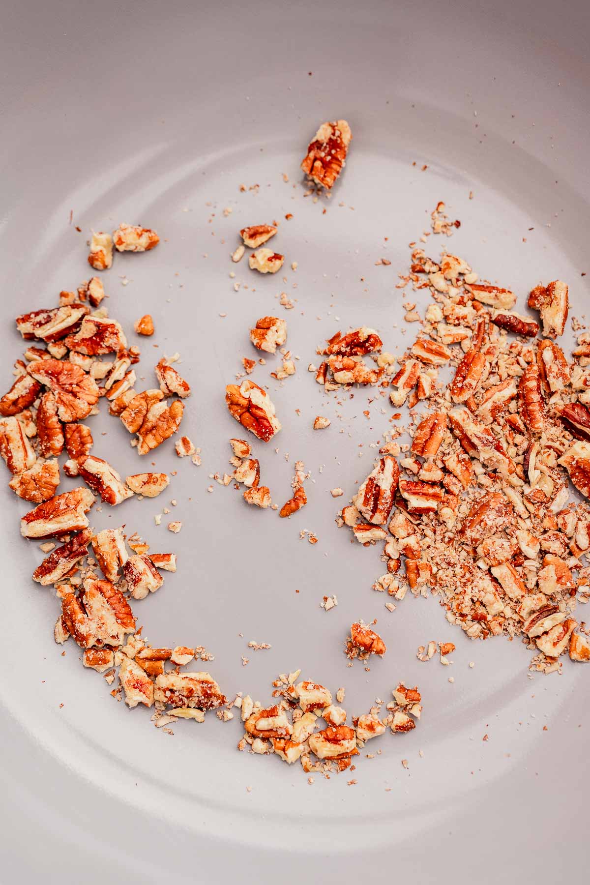 Chopped pecans scattered alongside chocolate balsamic glazed pears on a light gray surface.