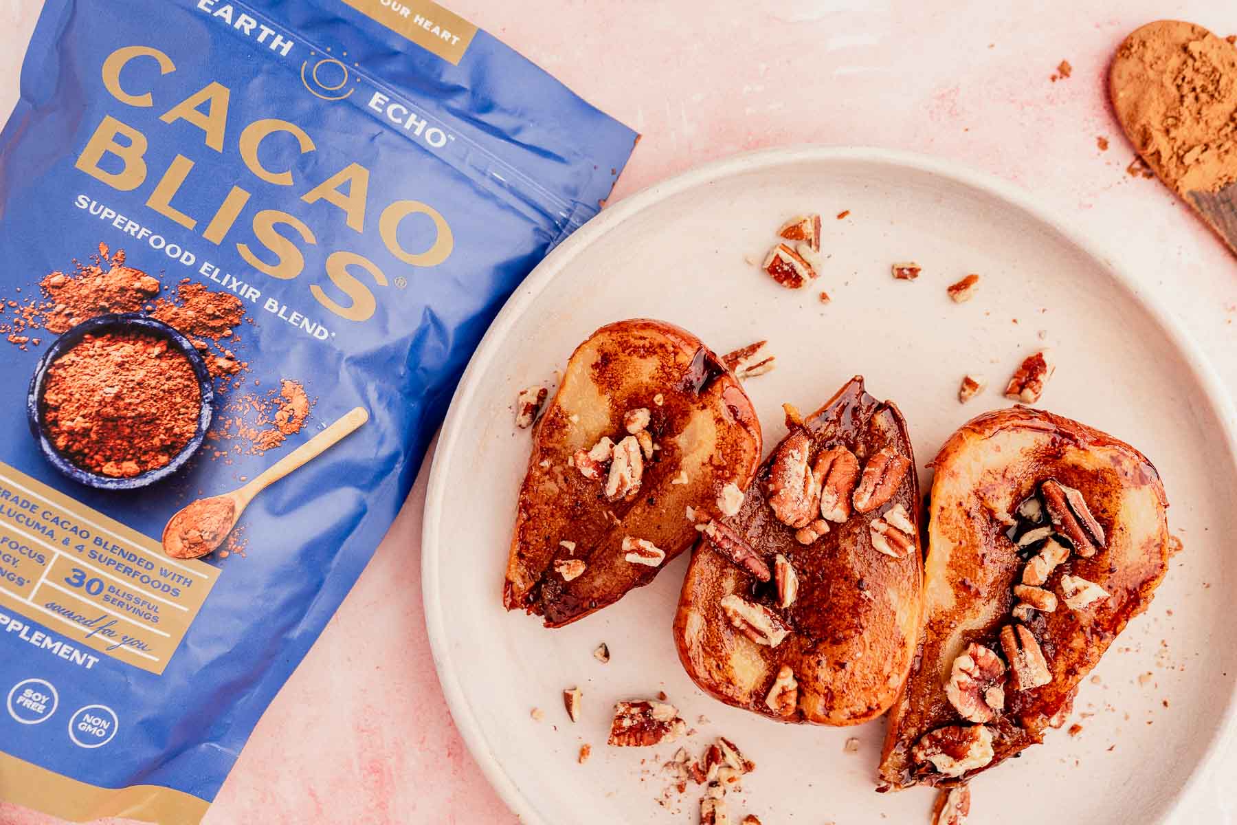 A plate with three slices of toast topped with pecans and a dusting of cacao powder sits enticingly beside a blue bag labeled "Cacao Bliss Superfood Elixir Blend." The sweet aroma hints at the delightful addition of chocolate balsamic glazed pears.