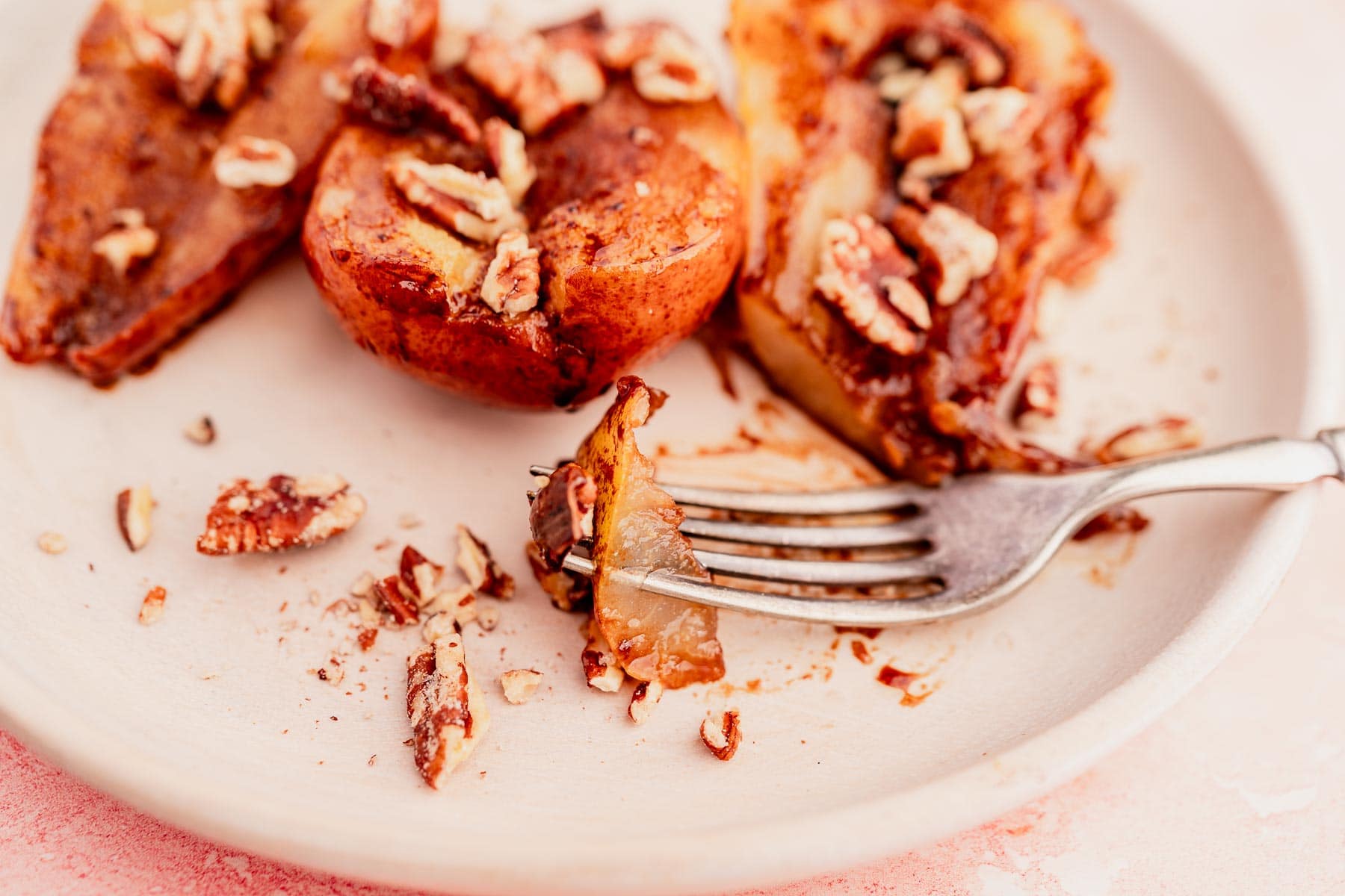A white plate showcases sliced caramelized pears drizzled with a rich chocolate balsamic glaze and topped with chopped pecans. A fork holds a piece of pear, inviting you to indulge.