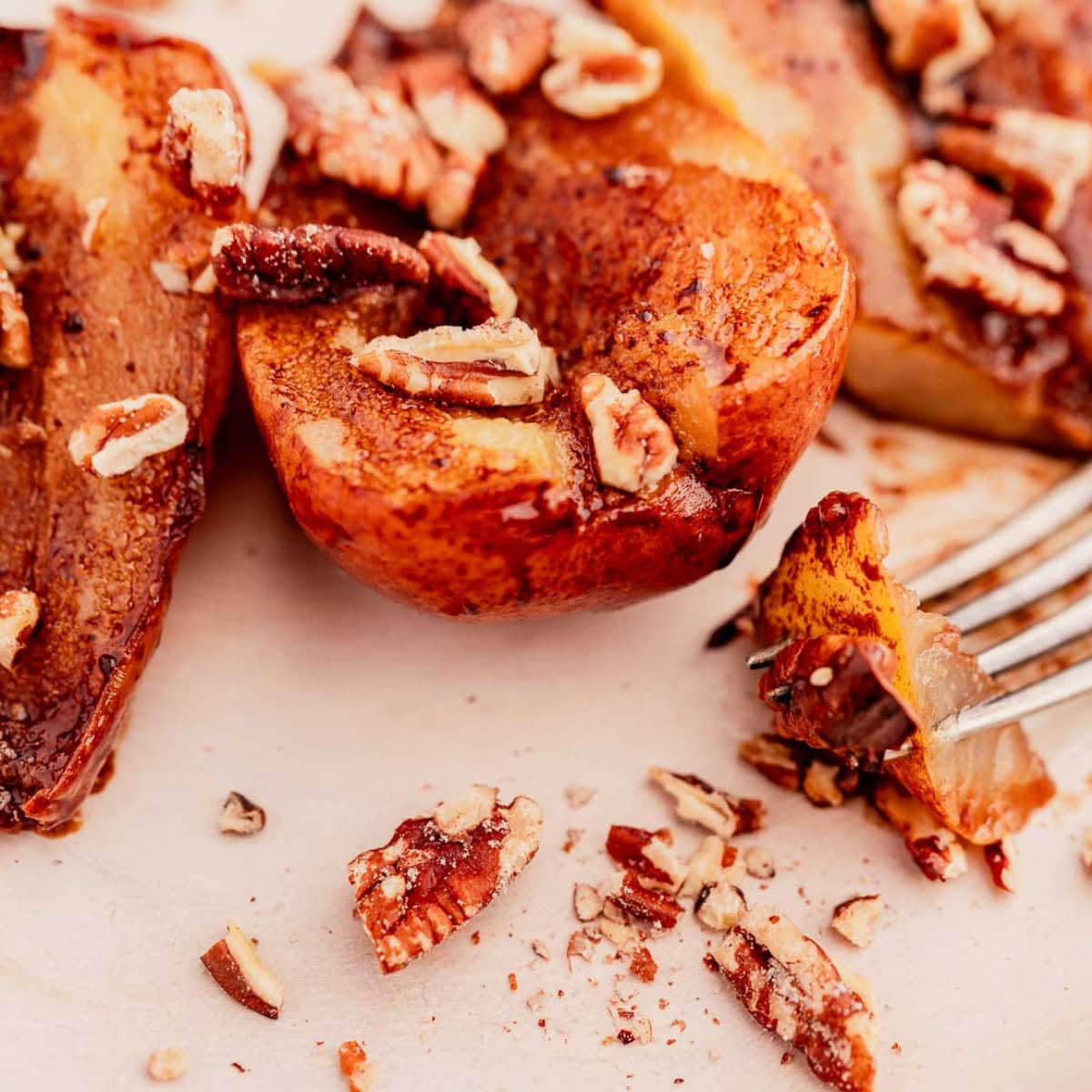 Roasted peaches topped with chopped pecans rest enticingly beside chocolate balsamic glazed pears, with a fork nearby on a light-colored surface.