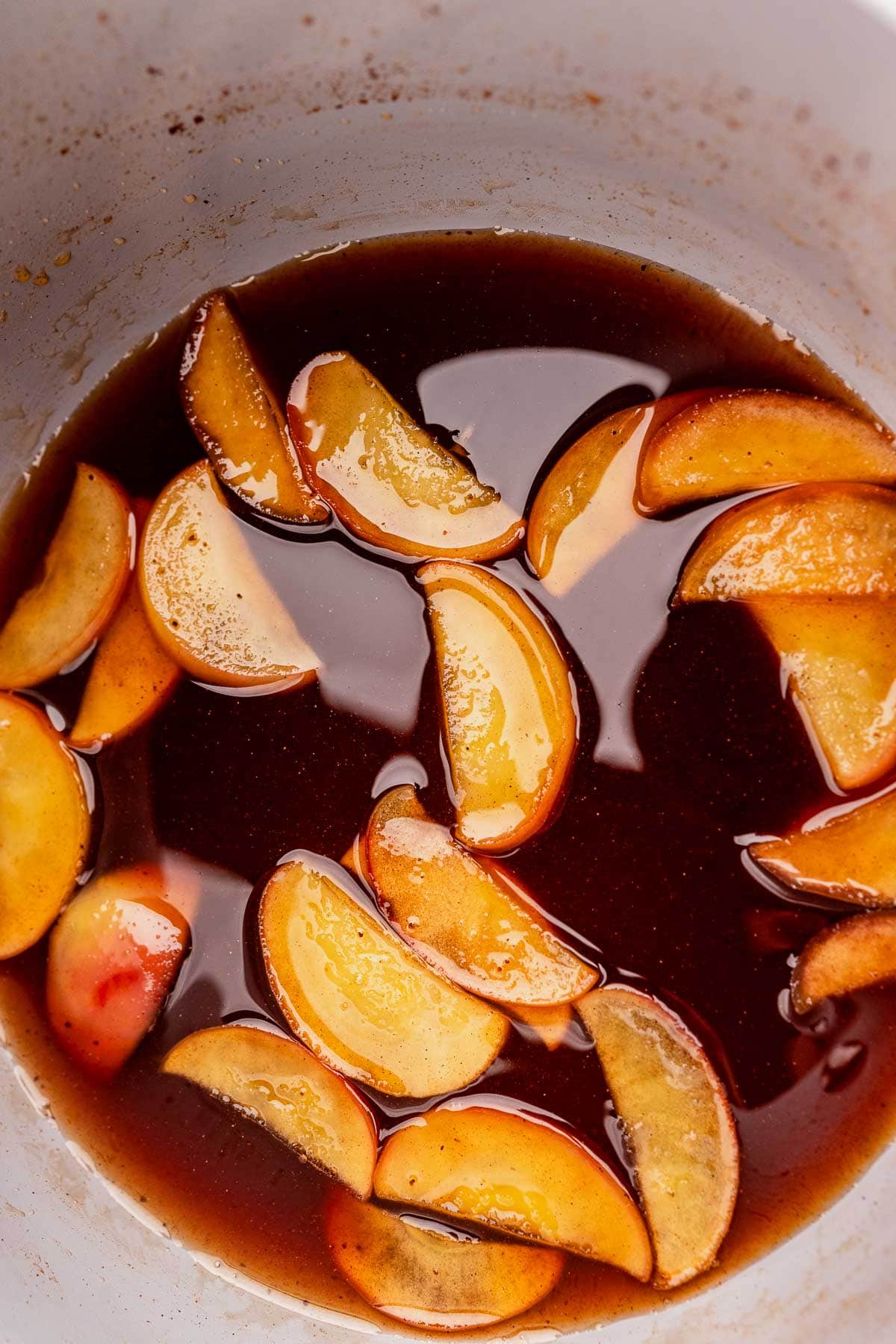 A white bowl cradles sliced peaches bathed in a warm brown liquid, subtly infused with the essence of Starbucks apple crisp syrup.