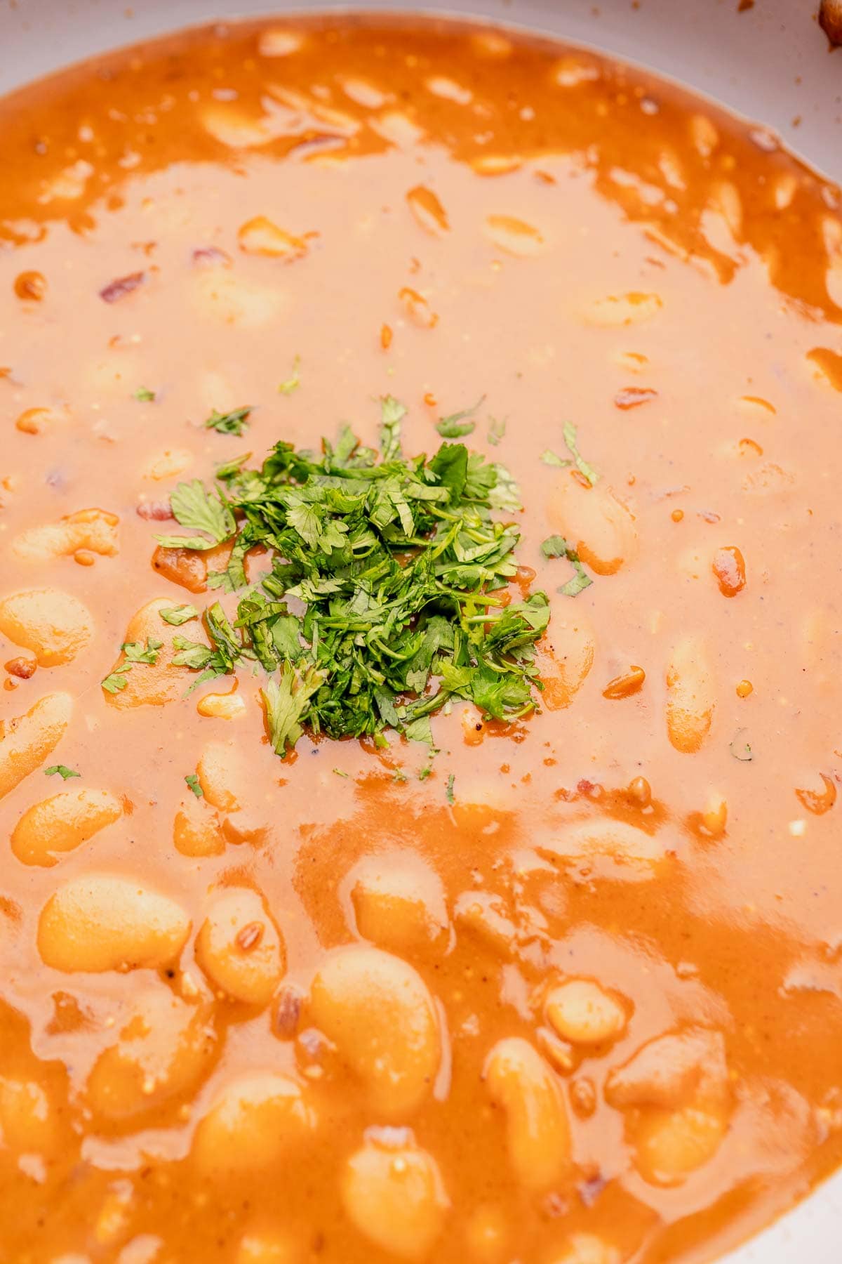 Fresh chopped cilantro rests atop a butter bean curry in a large pot.