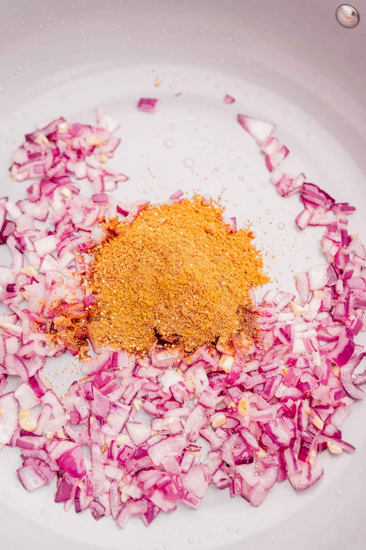 Sauteed red onions and ground spices in a pot.