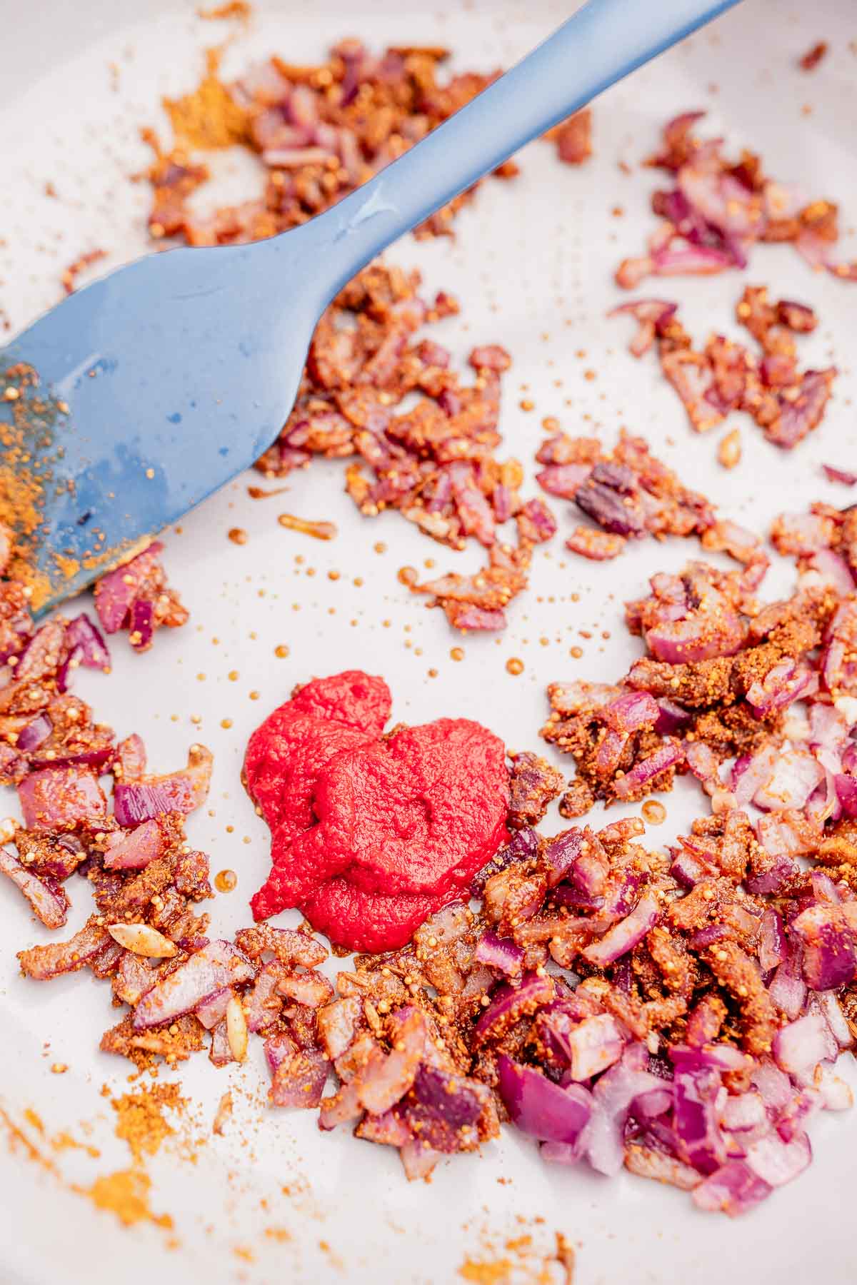 A dollop of red tomato pastes rests atop red onions and spices that are cooking.