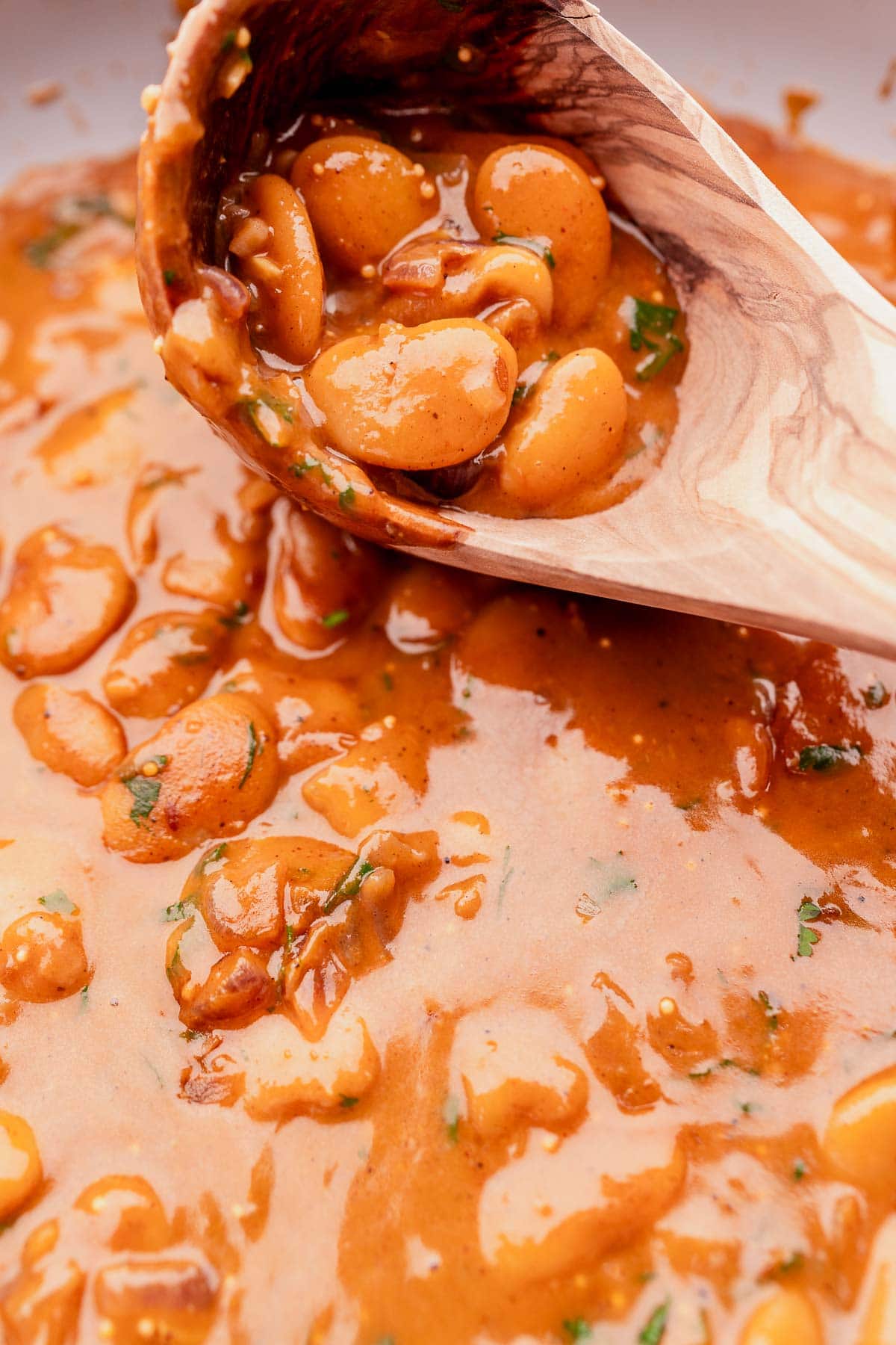 A wooden ladle scoops freshly made butter bean curry from a pot.
