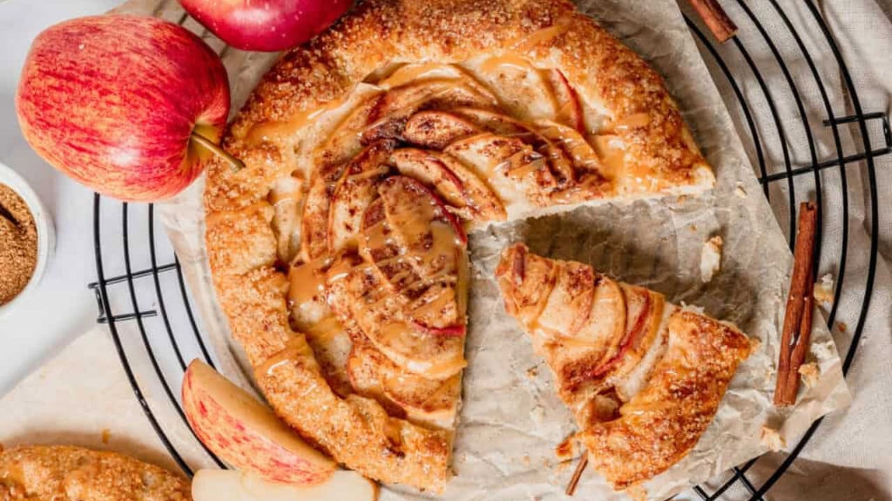 Overhead shot of an apple galette on parchment with fresh apples on the side.
