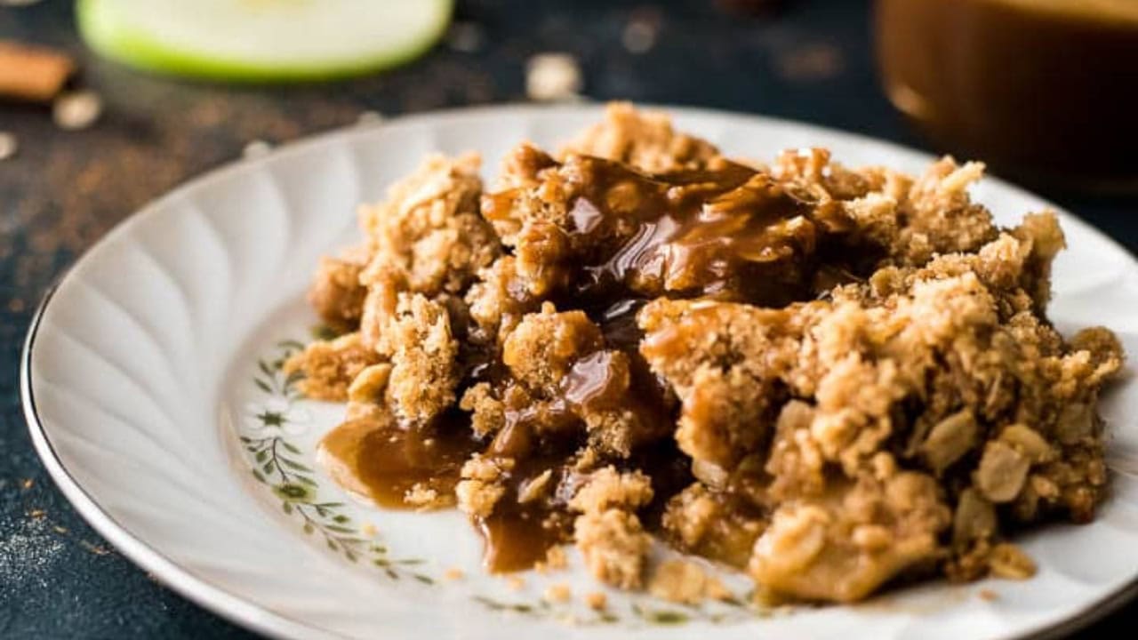 A butterscotch apple crumble in a cast iron skillet on a wooden cutting board.