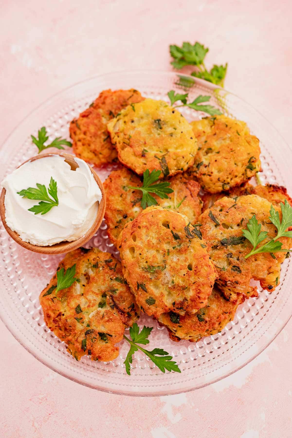 A plate of golden halloumi fritters, garnished with parsley, served alongside a small bowl of sour cream.