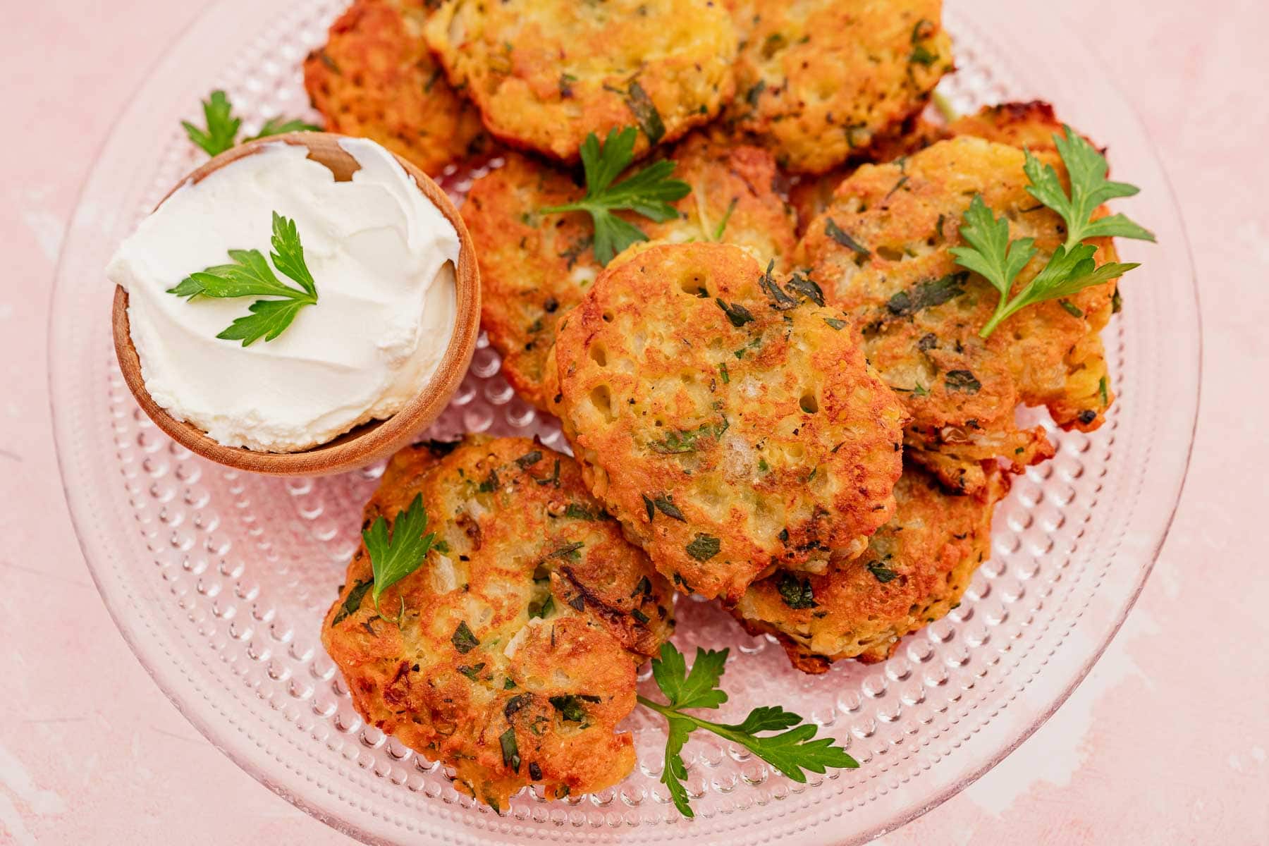 A plate of fried zucchini and halloumi fritters garnished with parsley, accompanied by a bowl of white dipping sauce topped with parsley.