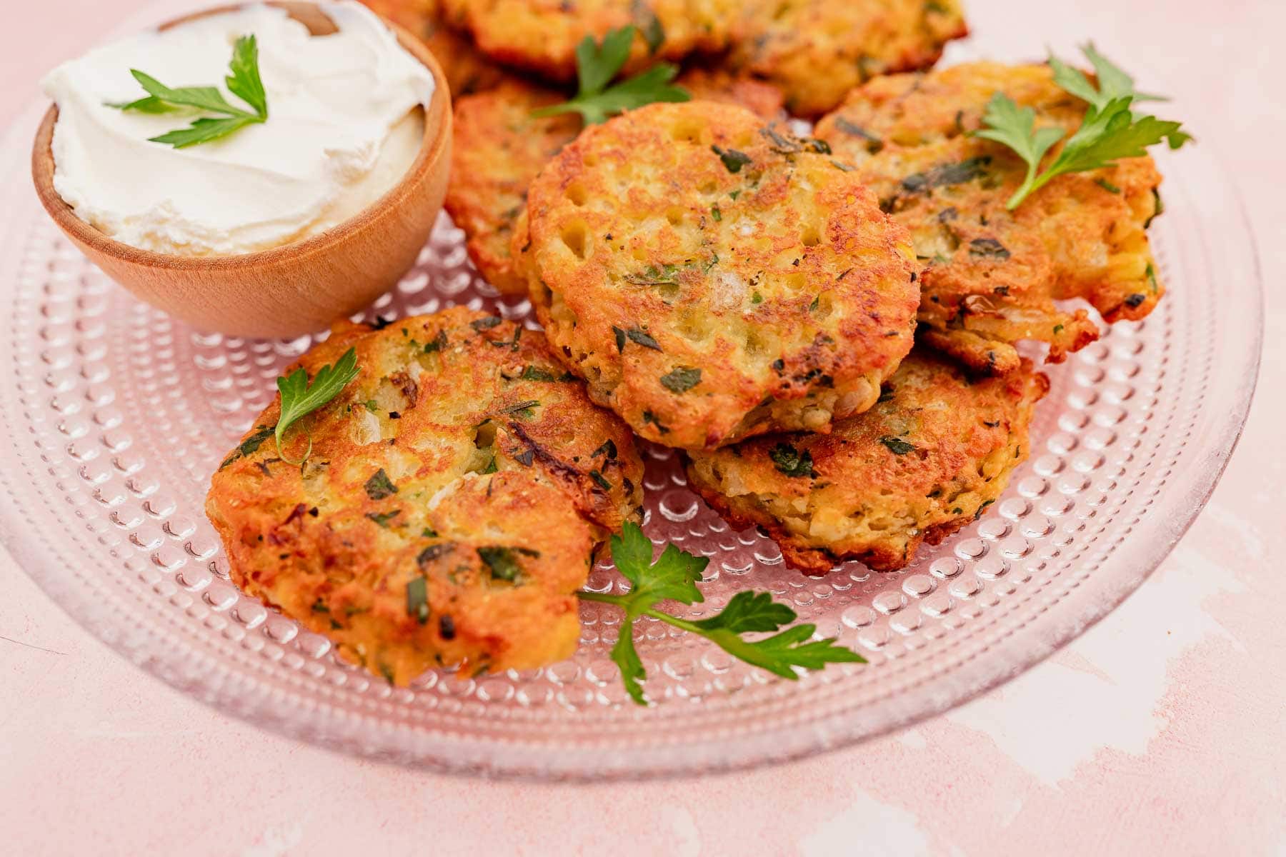 A plate of crispy vegetable and halloumi fritters with fresh herbs, served alongside a small bowl of sour cream.