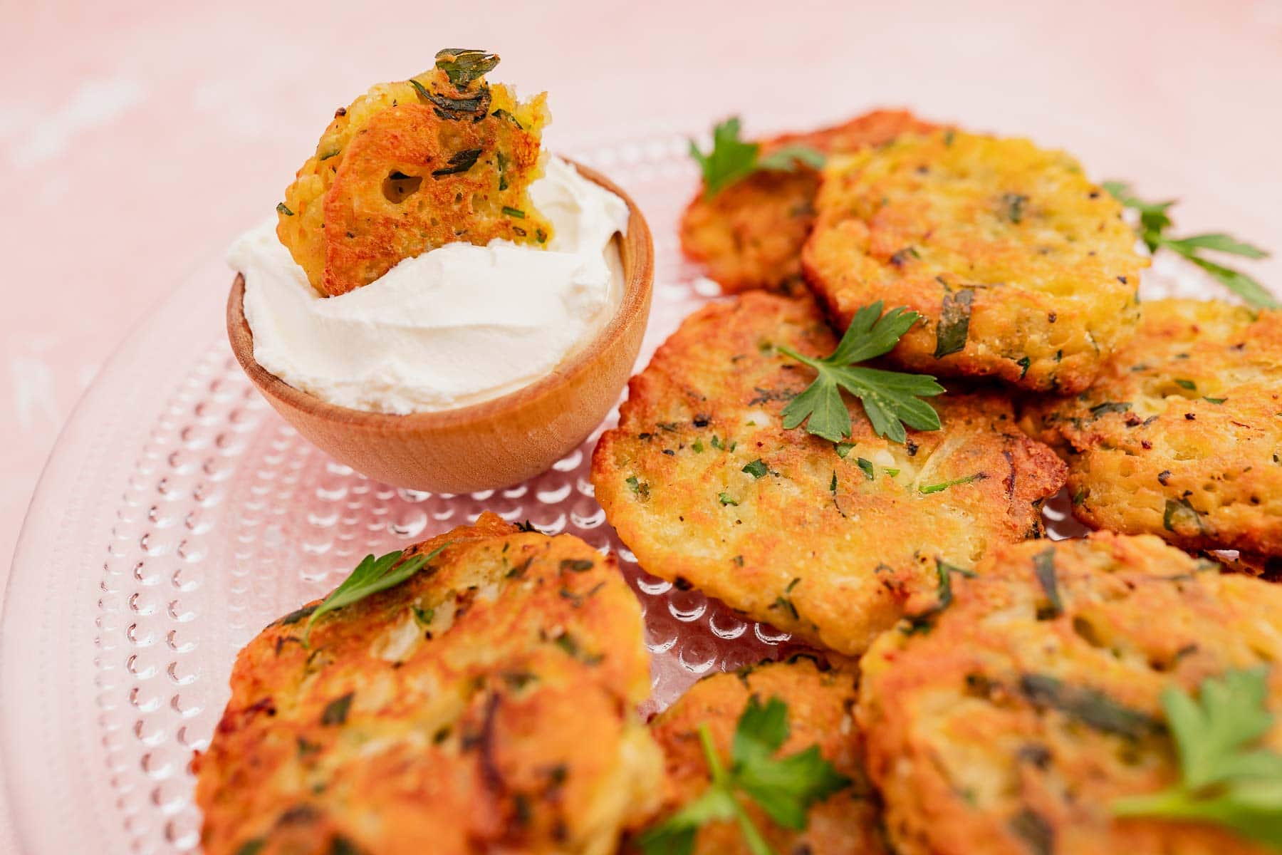 A plate of vegetable and halloumi fritters garnished with parsley is served with a small bowl of creamy dip.