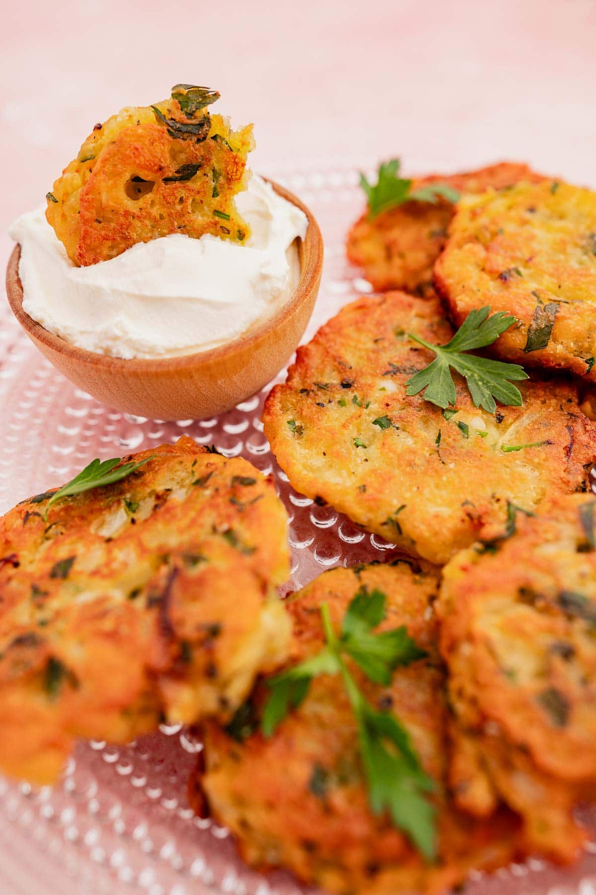 A plate of golden zucchini and halloumi fritters with parsley garnish, accompanied by a small bowl of sour cream.