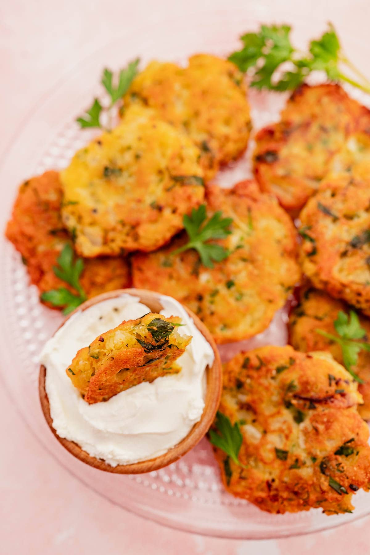 Plate of vegetable and halloumi fritters with fresh herbs, one piece dipped in a small bowl of sour cream or yogurt.