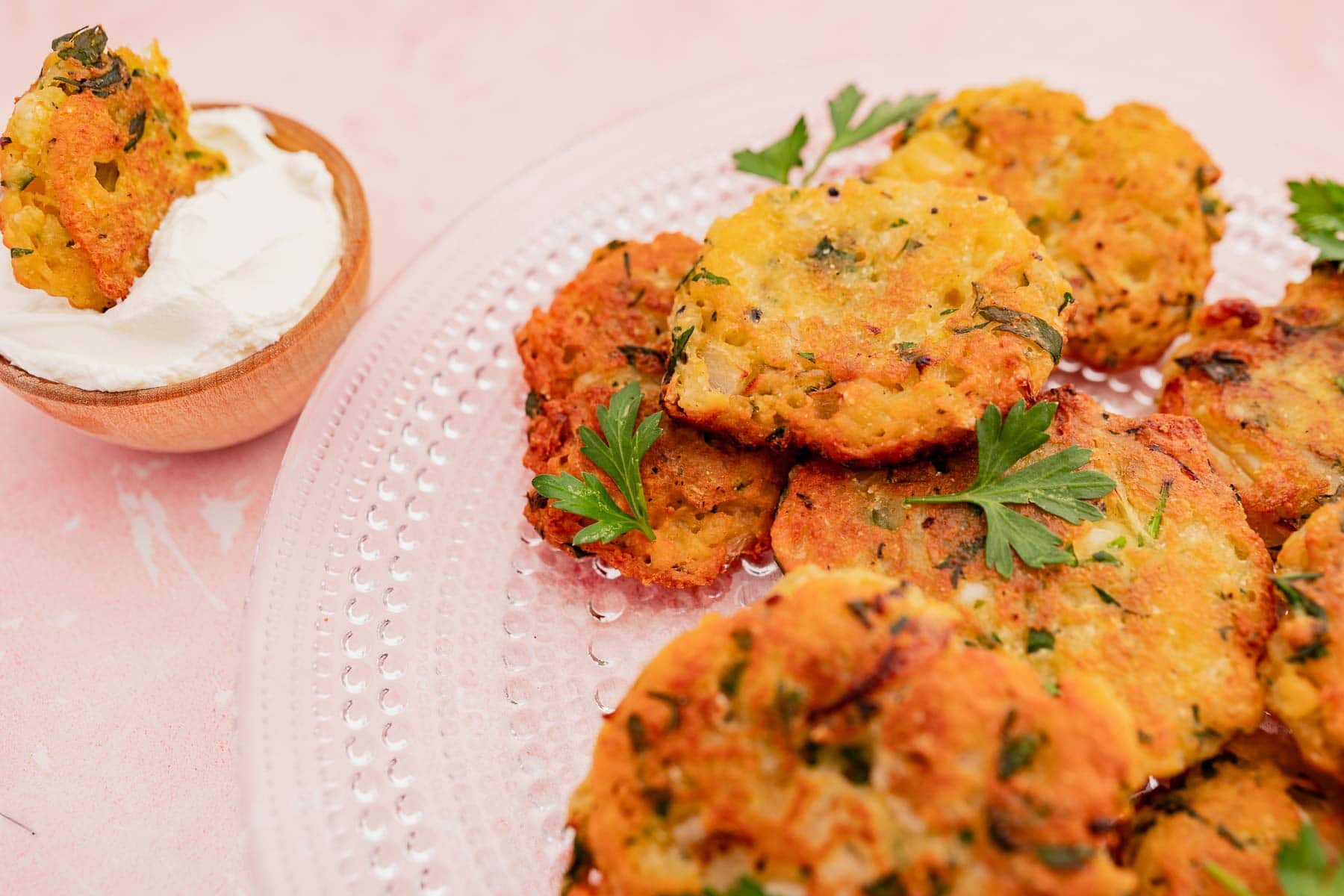 A plate of seasoned halloumi fritters garnished with parsley rests next to a wooden bowl of sour cream.