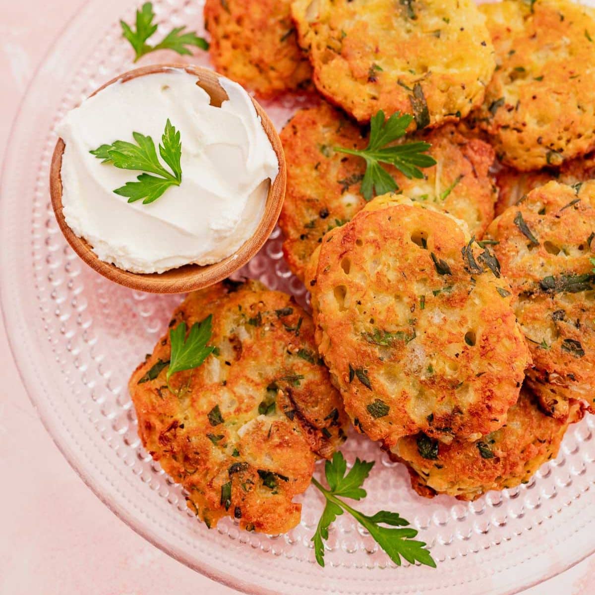 A plate of golden zucchini fritters topped with parsley, served with a small bowl of creamy dip.