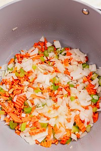Chopped onions, carrots, and celery are shown in a pot, ready to be cooked as the flavorful base for a comforting Jamaican pumpkin soup.