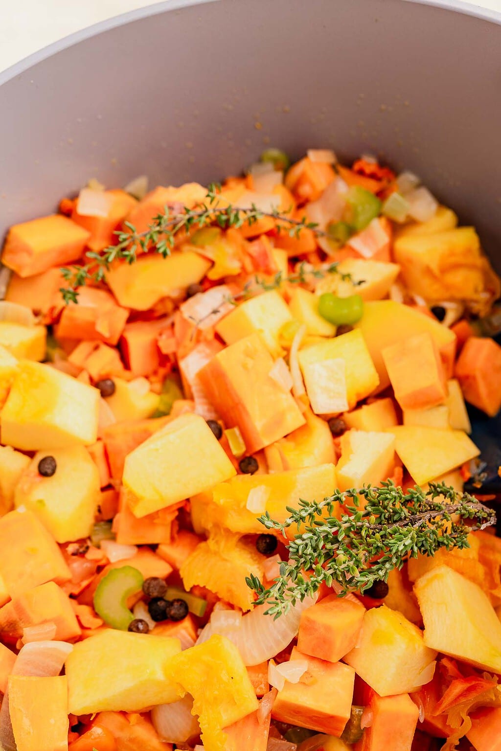 Chopped root vegetables, celery, onion, and herbs, including thyme, in a pot, ready for cooking a flavorful Jamaican pumpkin soup.