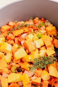 Chopped root vegetables, celery, onion, and herbs, including thyme, in a pot, ready for cooking a flavorful Jamaican pumpkin soup.