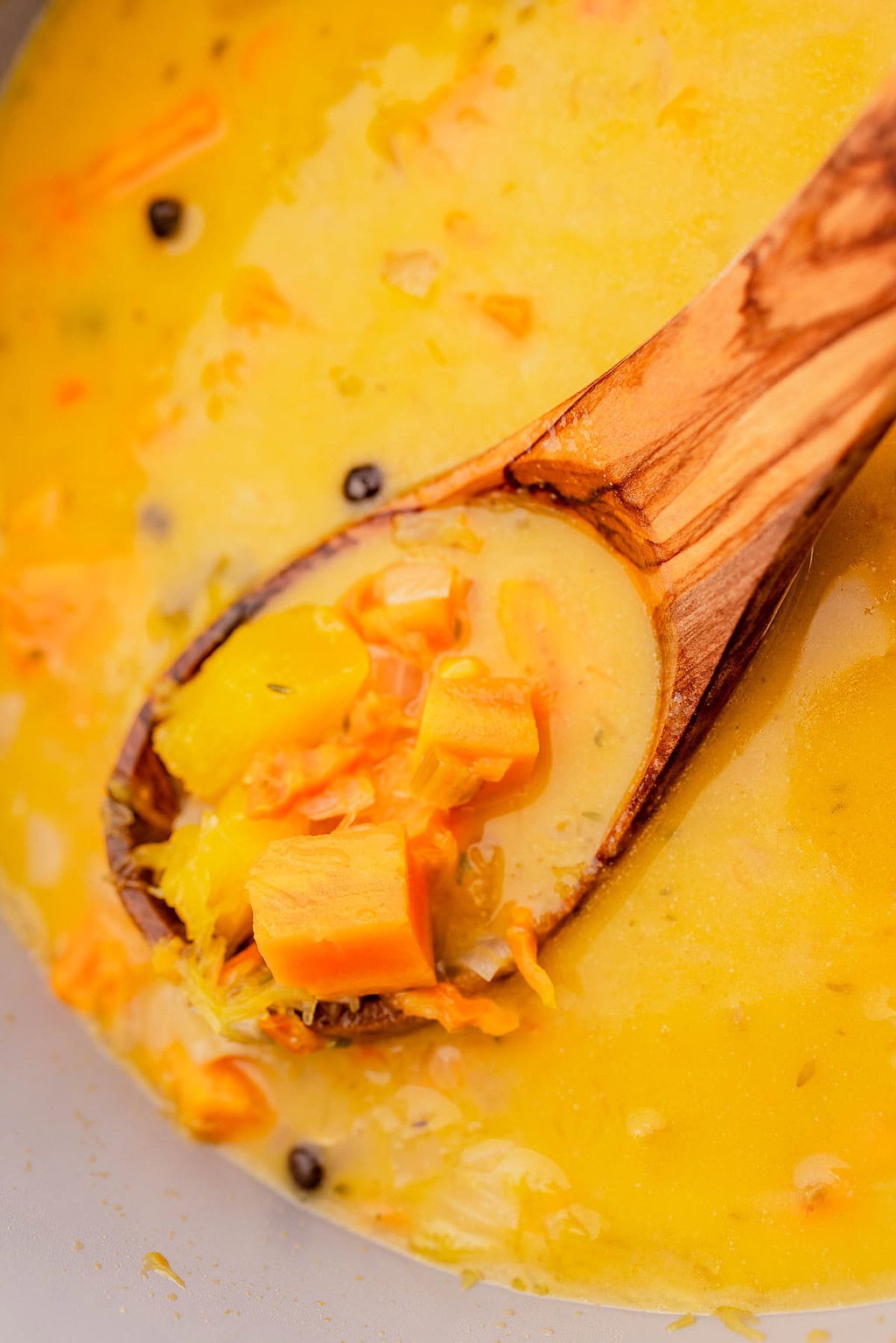 Close-up of a wooden spoon holding chunks of yellow and orange vegetables in a creamy yellow jamaican pumpkin soup.