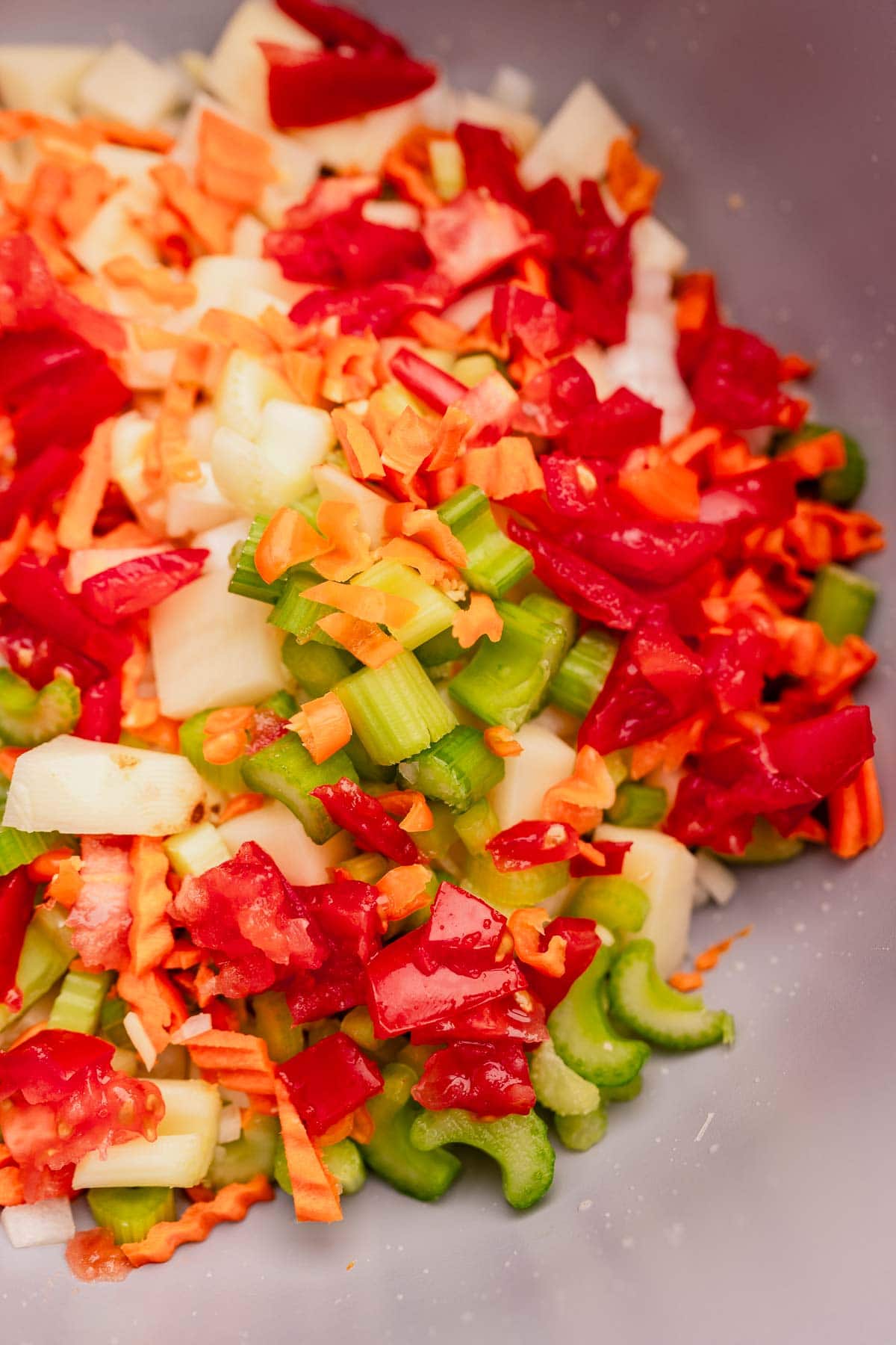 Close-up of chopped vegetables, including celery, red bell pepper, carrots, and onions, in a bowl ready to be mixed with lentejas.
