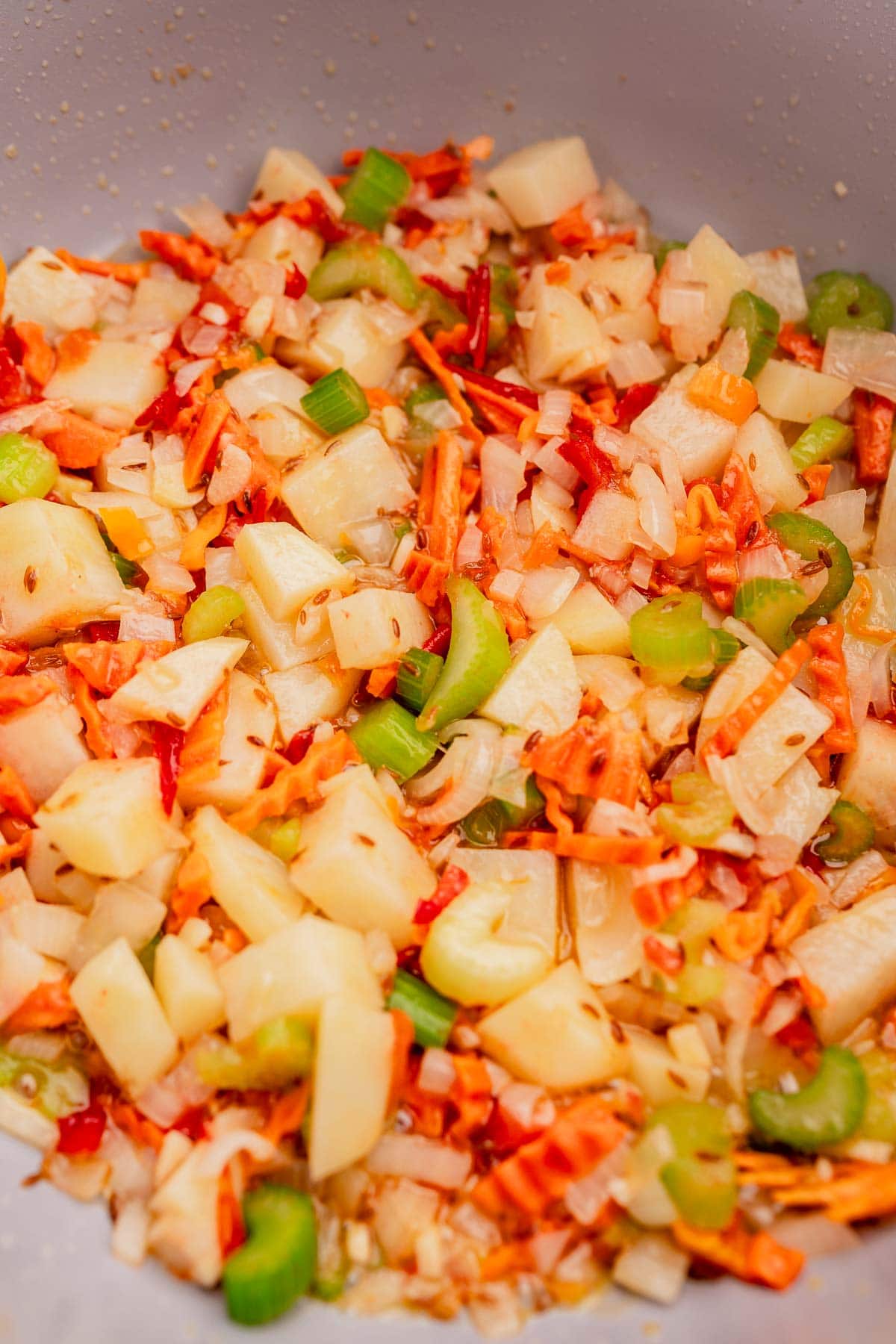 A close-up of a colorful vegetable stir-fry featuring diced carrots, potatoes, celery, onions, and hearty lentejas simmering together in a pan.