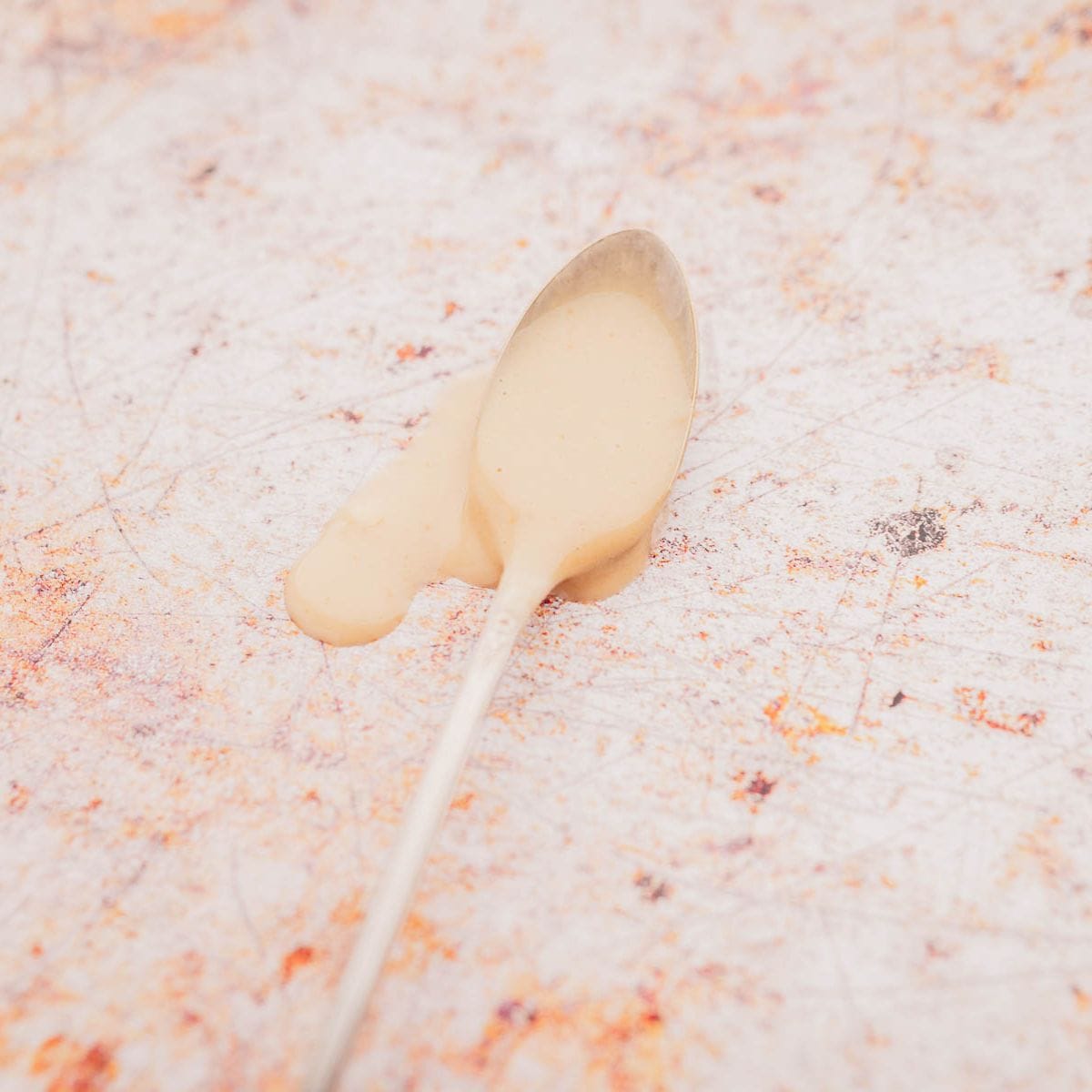 A spoon with beige miso mayo on a textured, speckled surface.