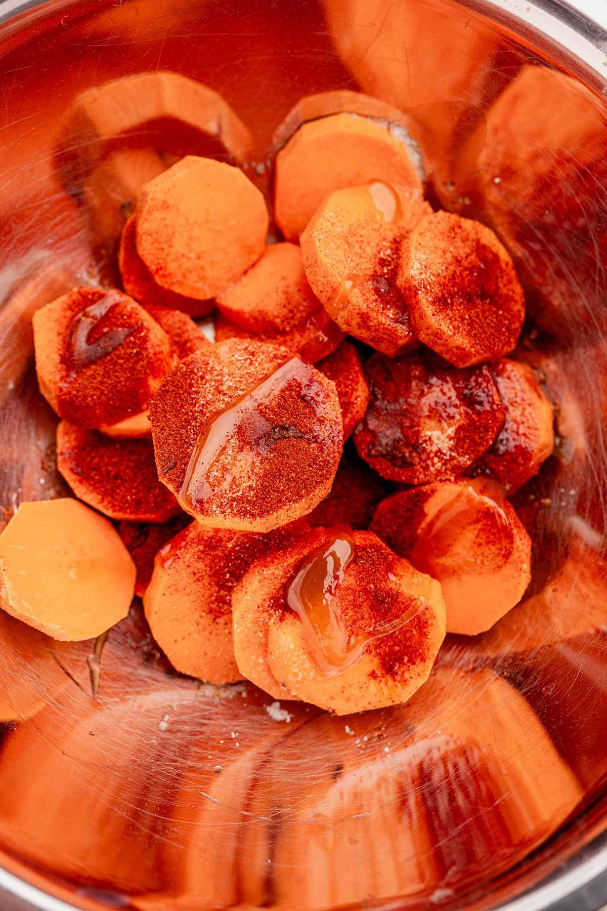 Sliced sweet potatoes with seasoning and oil are ready to transform into delicious baked sweet potato slices in a metal bowl.