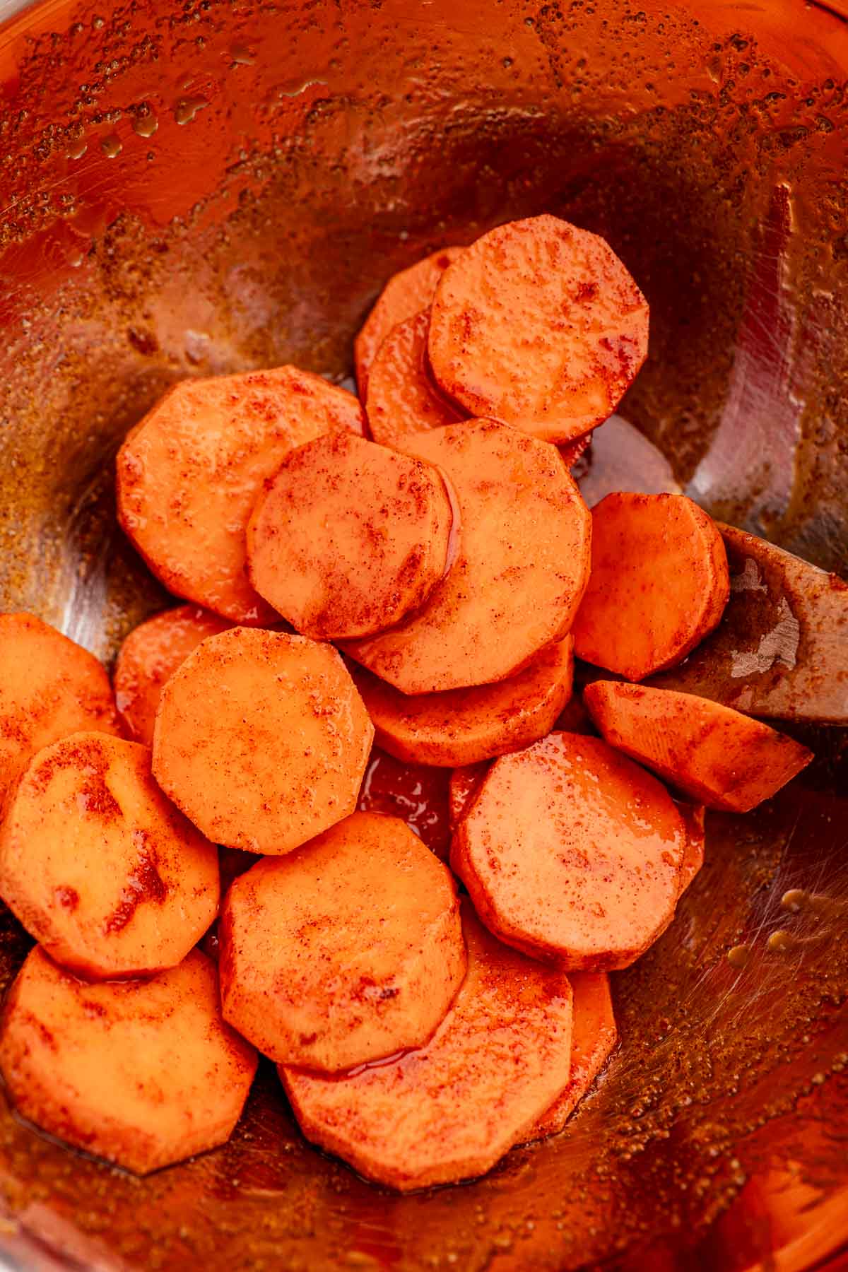 Baked sweet potato slices are tossed with spices in a metal mixing bowl, creating a flavorful dish.