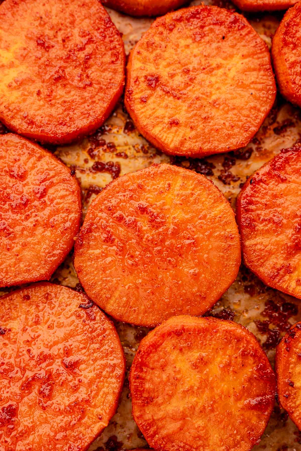 Close-up of baked sweet potato slices, golden brown with a slightly crispy texture, arranged on a baking sheet.