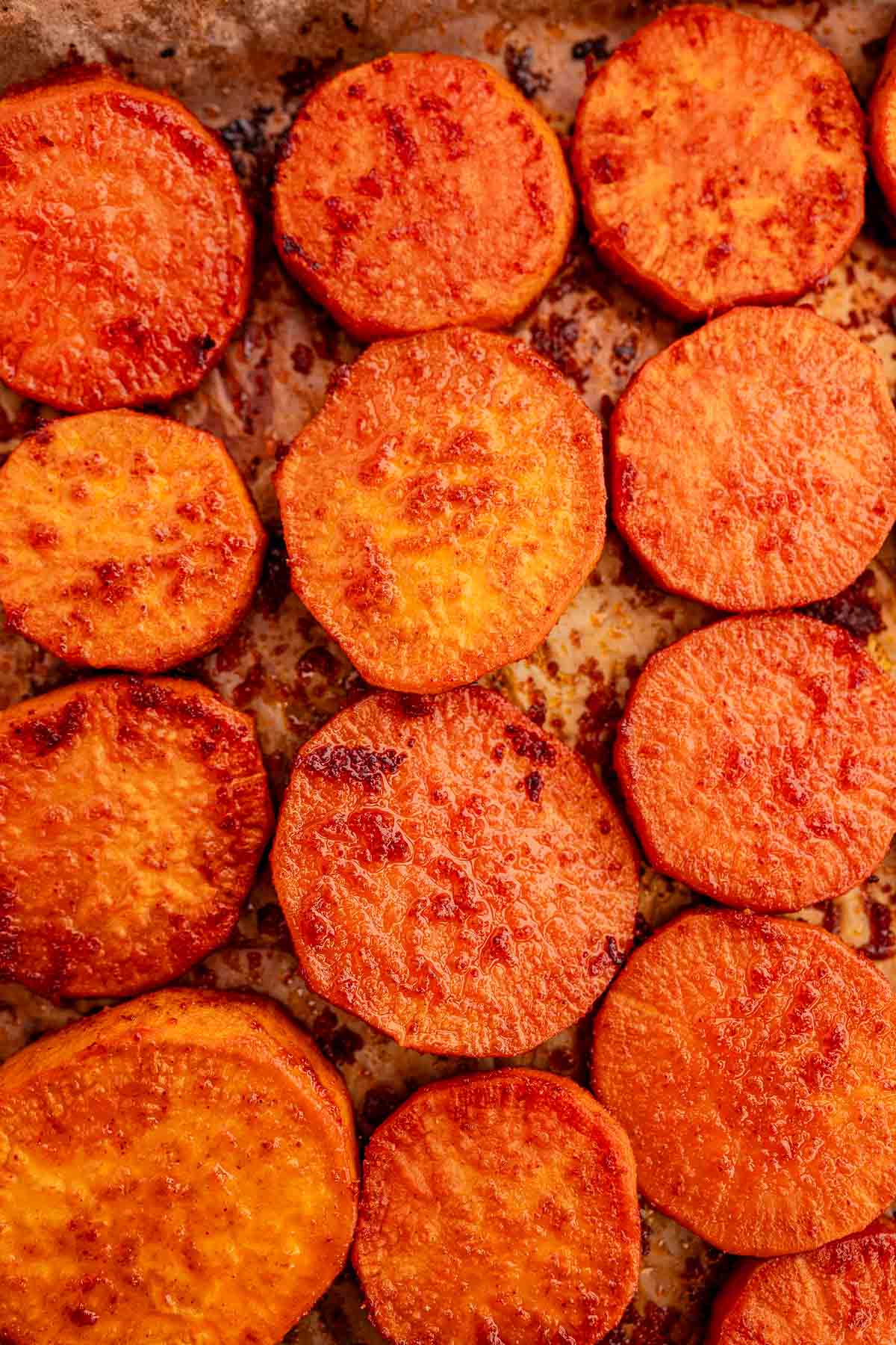 A close-up of baked sweet potato slices on a baking sheet. The slices are golden-brown with a slightly crispy texture.