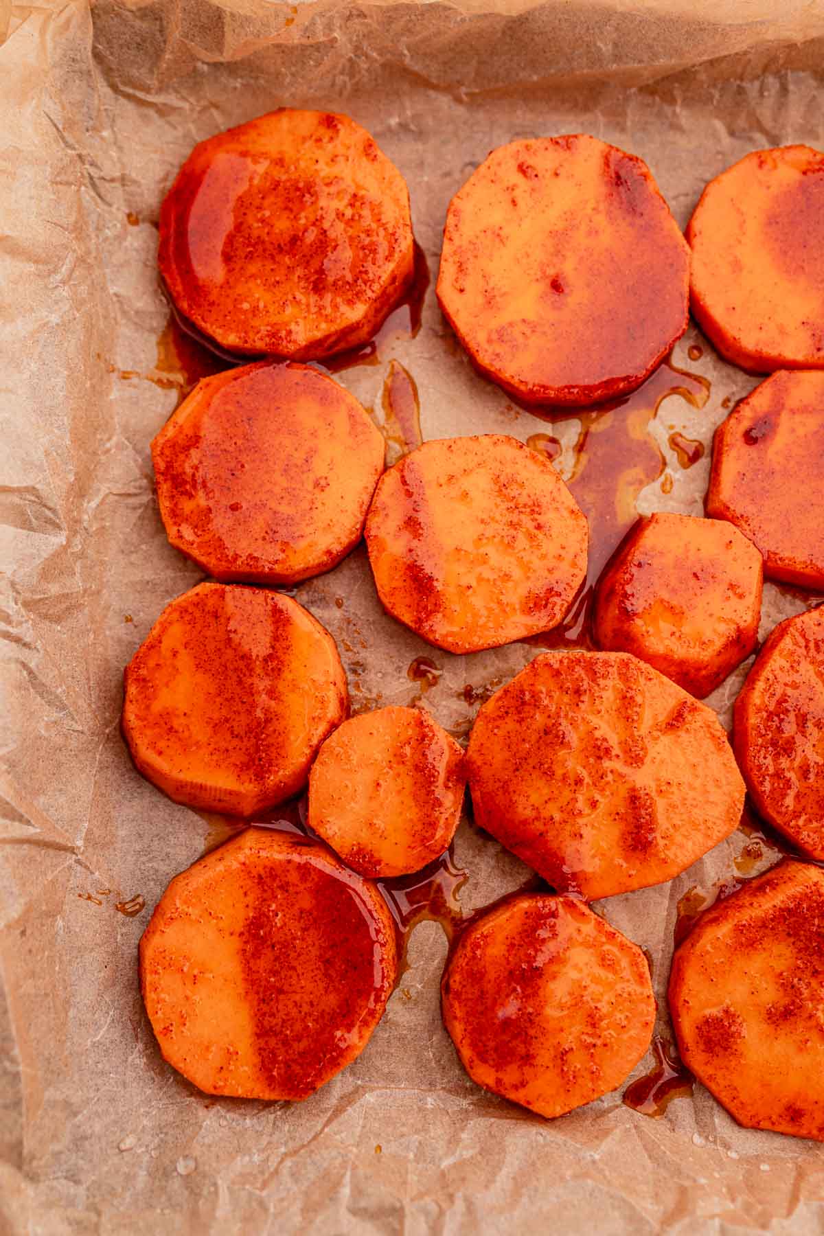 Baked sweet potato slices, seasoned to perfection, are spread evenly on parchment paper.