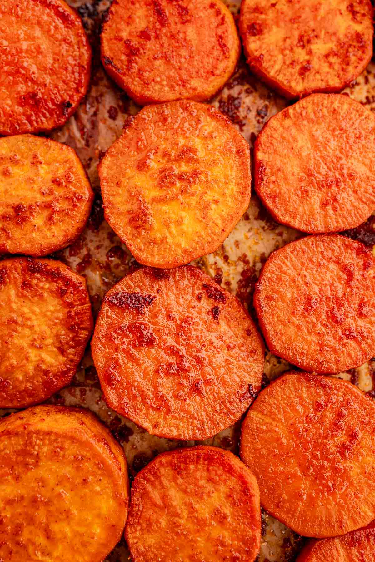 A close-up of evenly spaced baked sweet potato slices reveals a crispy, caramelized surface on a baking sheet.